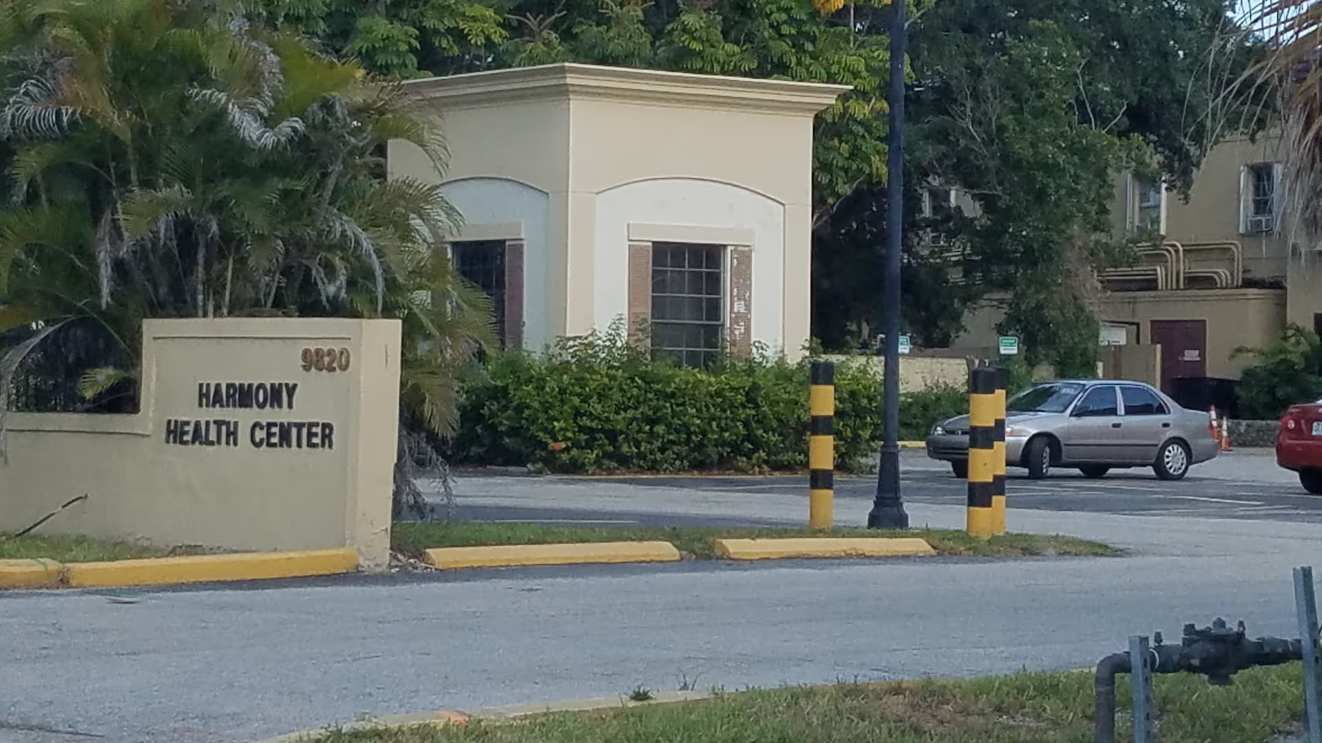 Exterior view of Harmony Health Center entrance with sign, shrubs, and parked cars.