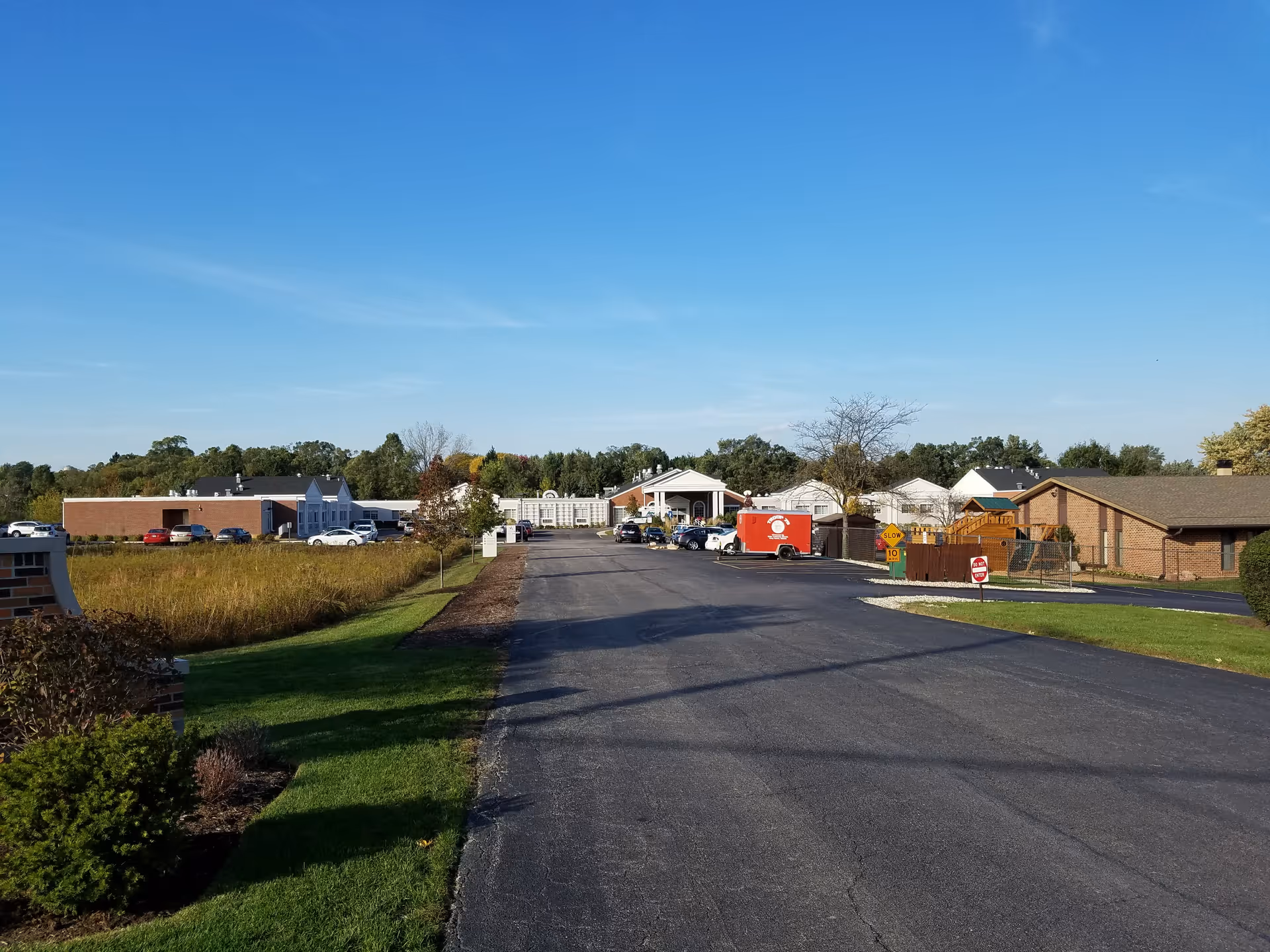 Wide view of a senior living campus entrance with parking and low-rise buildings.