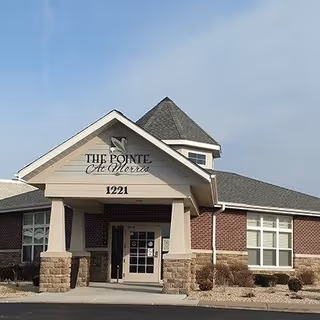 Front exterior view of The Pointe At Morris facility building with a peaked roof, brick and stone facade, and entrance door under a covered porch with the address number 1221.