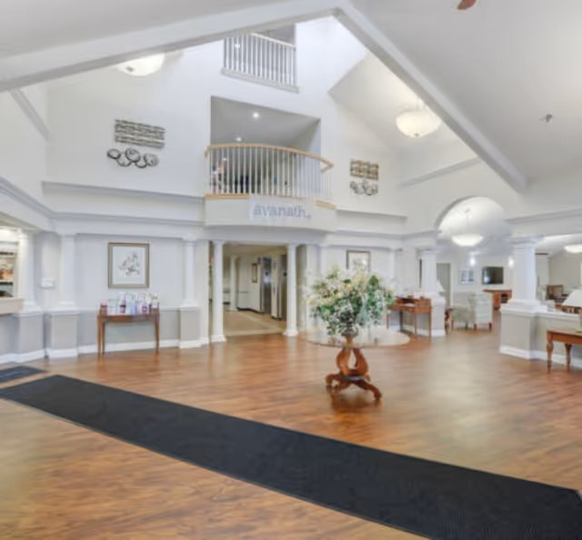 Spacious white lobby with a wooden floor, centerpiece plant, and arched doorway in senior living facility.