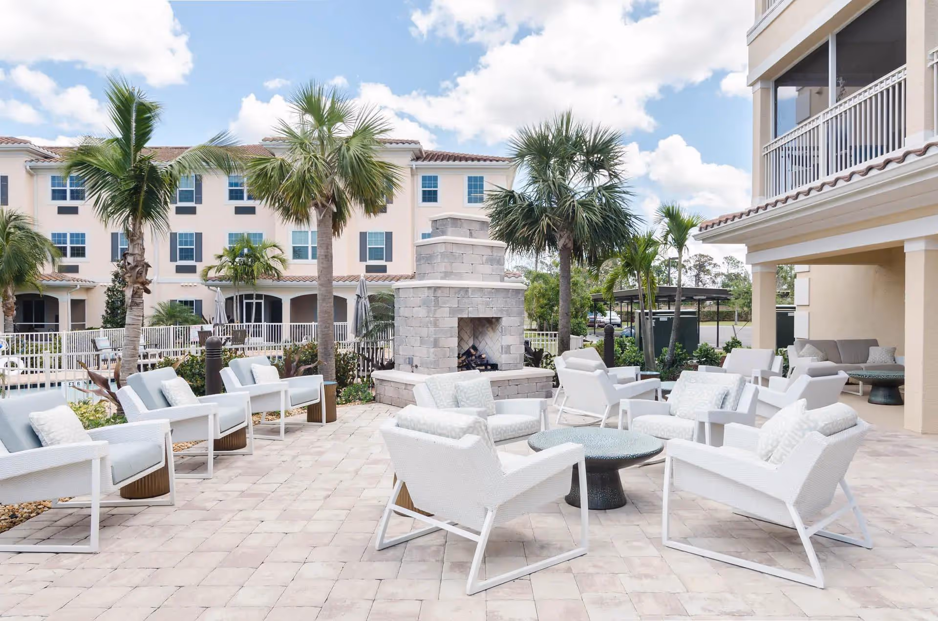 Outdoor lounge area with white chairs surrounding a stone fireplace and palm trees