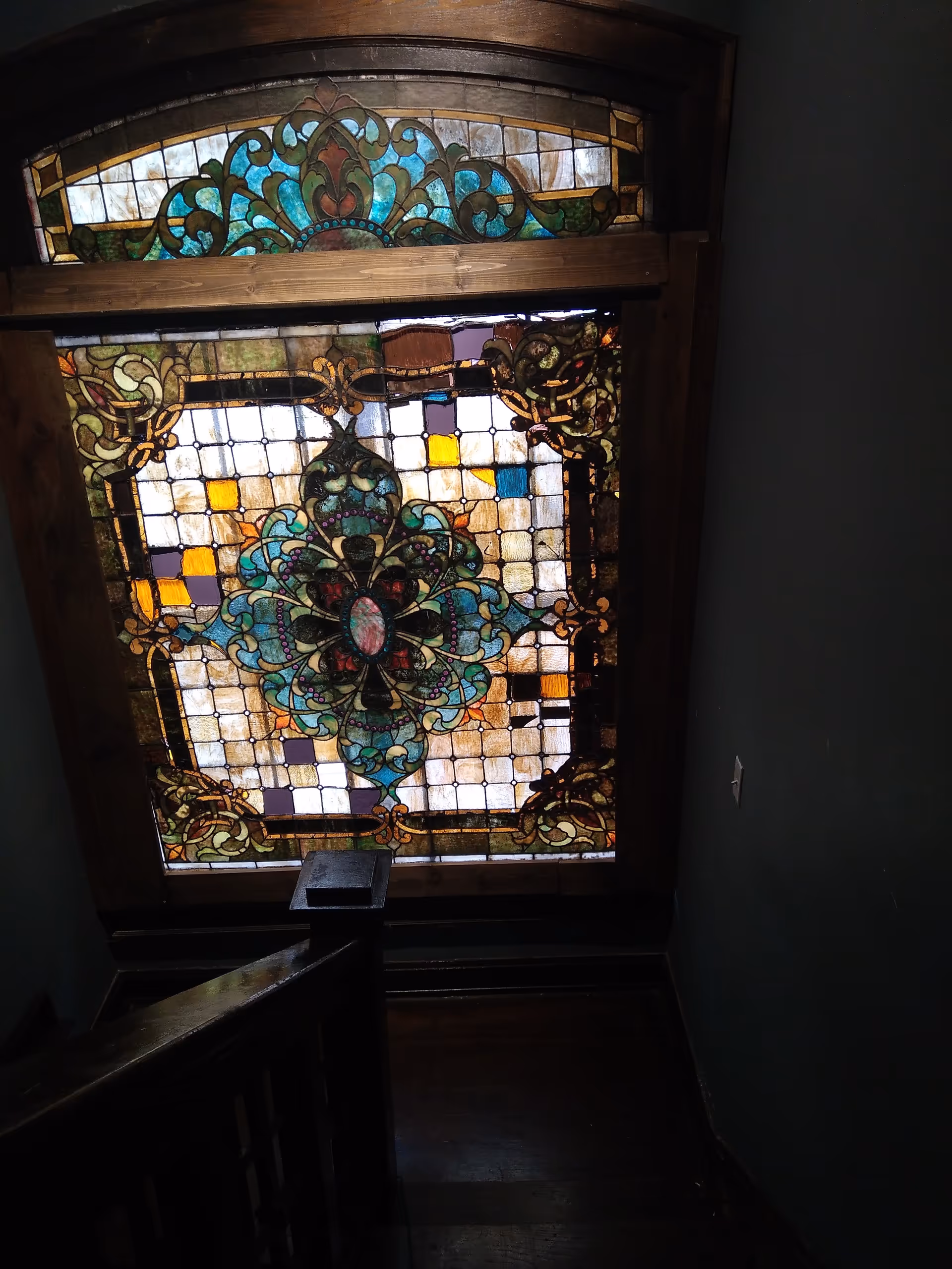 Dark stairwell with a large colorful stained-glass window at the landing.