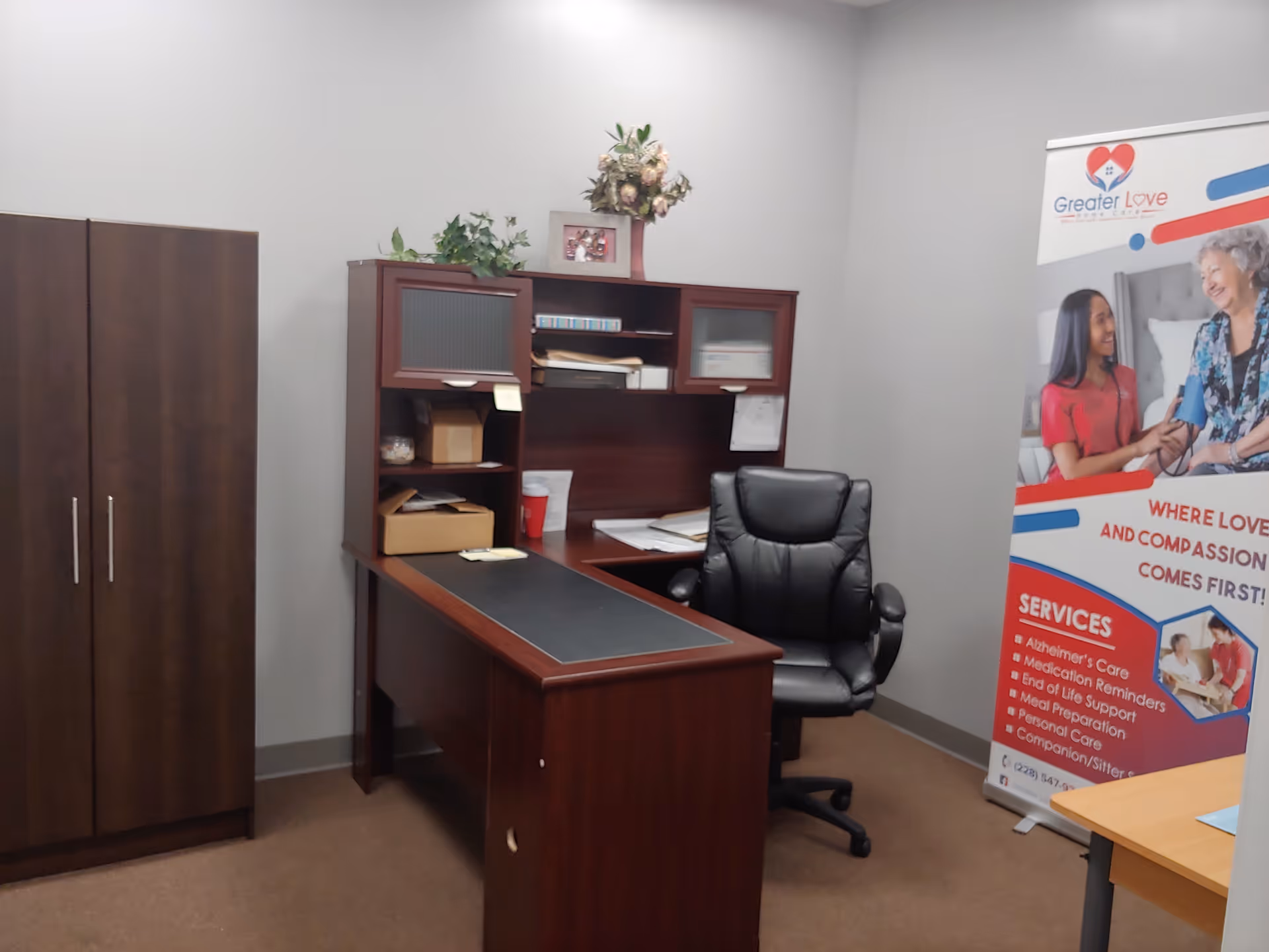 Office workspace with desk, chair, cabinets, and a Greater Love banner.
