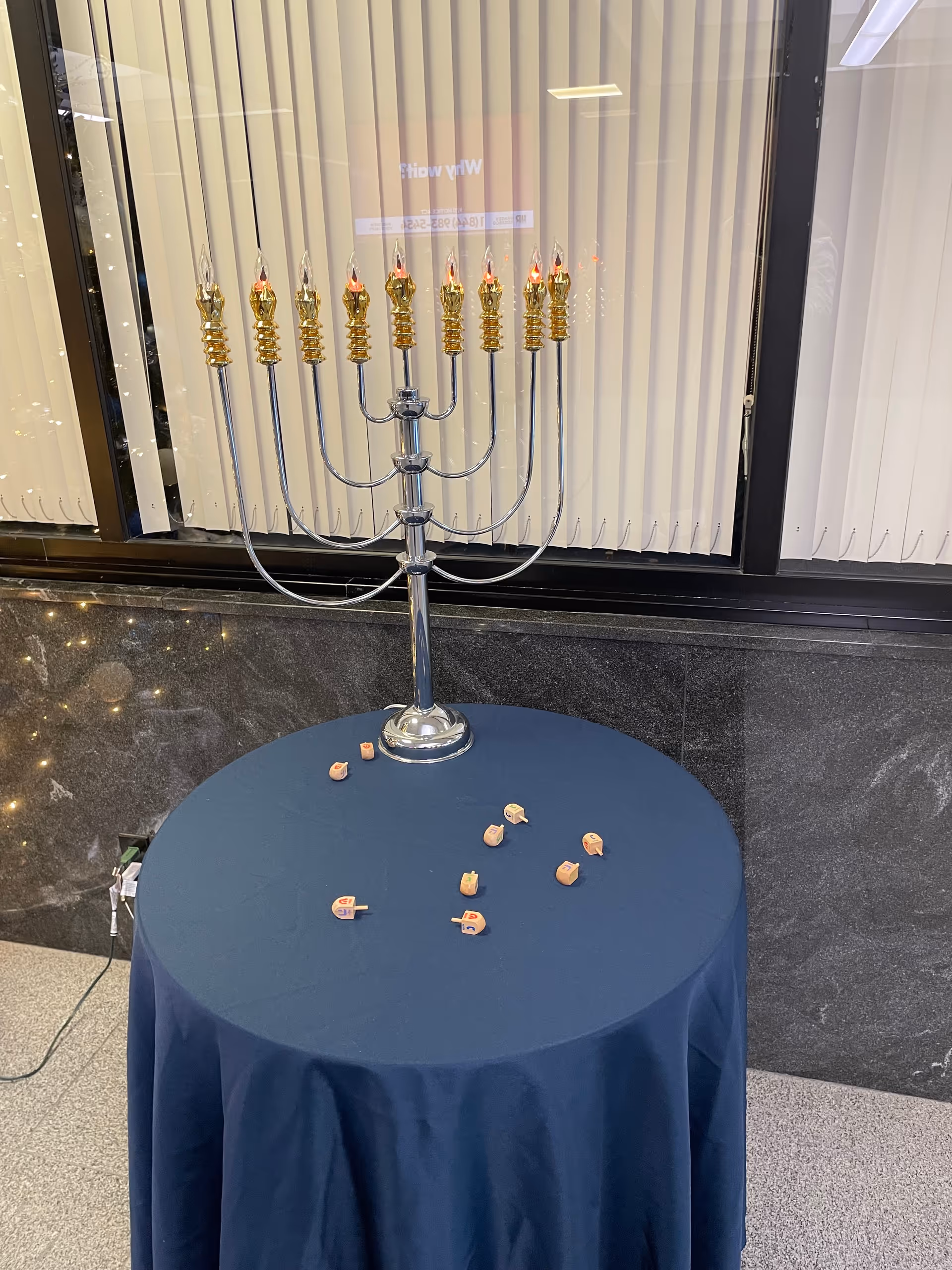 A silver menorah with lit candles sits on a blue tablecloth-covered round table indoors.