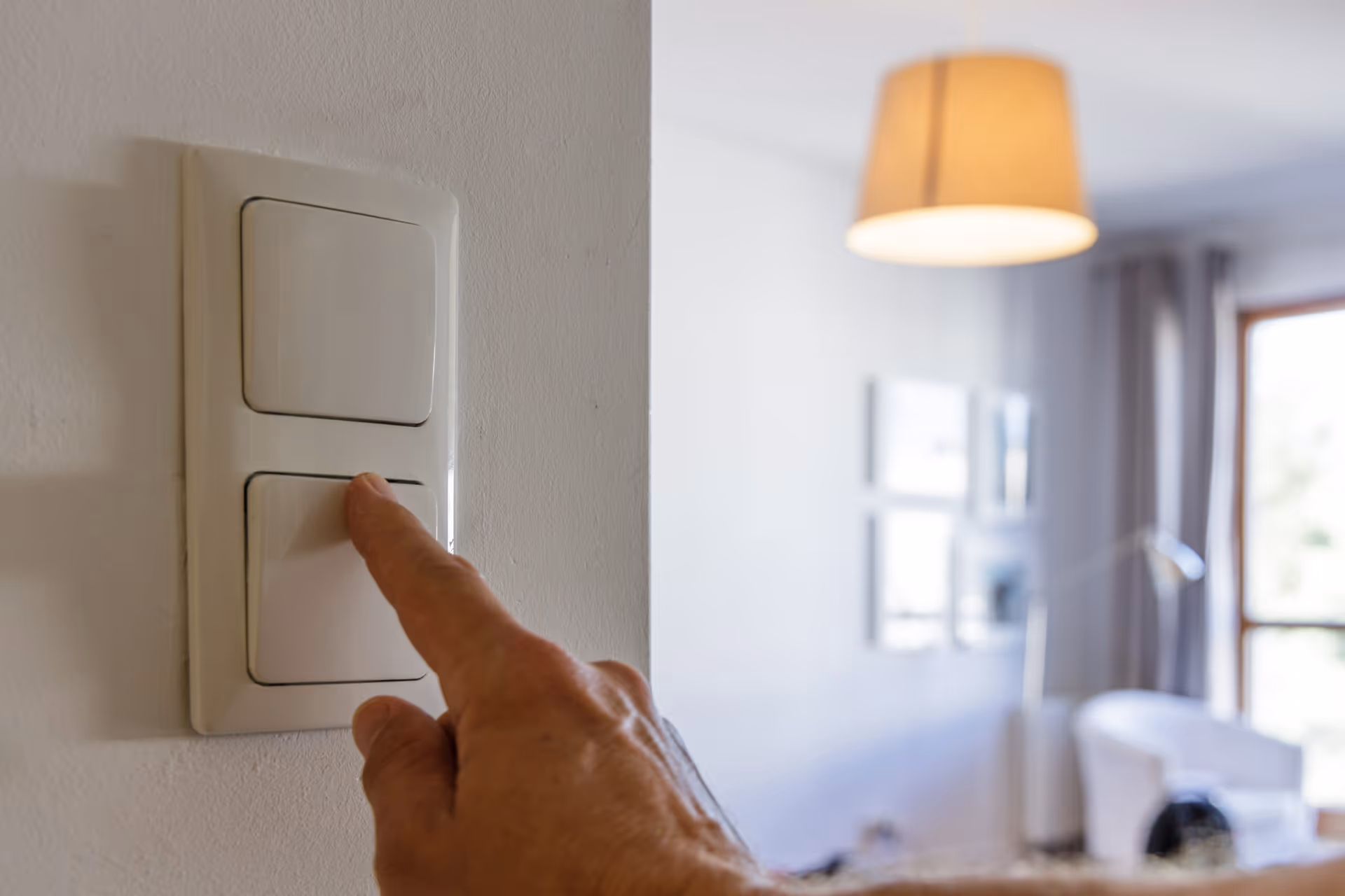 Close-up of a hand pressing a light switch in a bright living room.