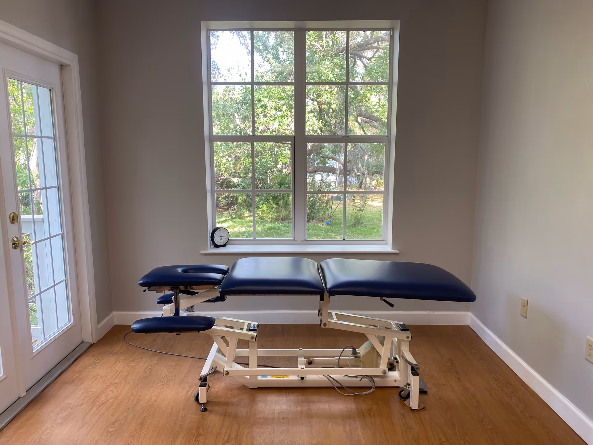 A blue therapy table sits in a bright, empty treatment room with a large window.