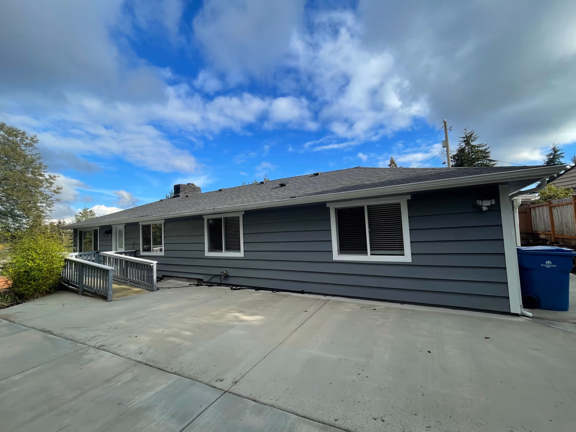 Exterior of a single-story blue-gray senior facility with ramp, windows, and a concrete driveway.