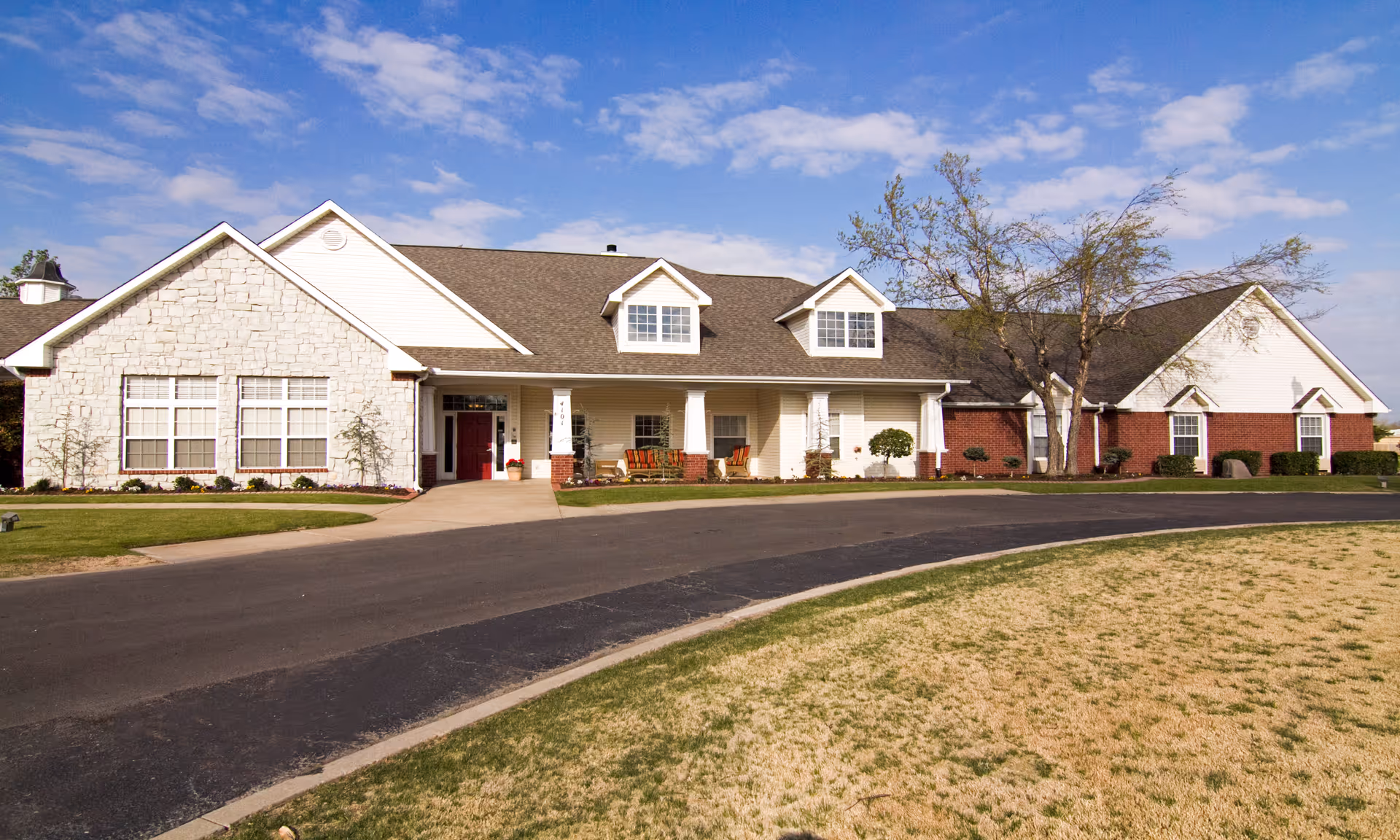 Exterior view of a long, welcoming assisted living facility with a driveway and front porch.