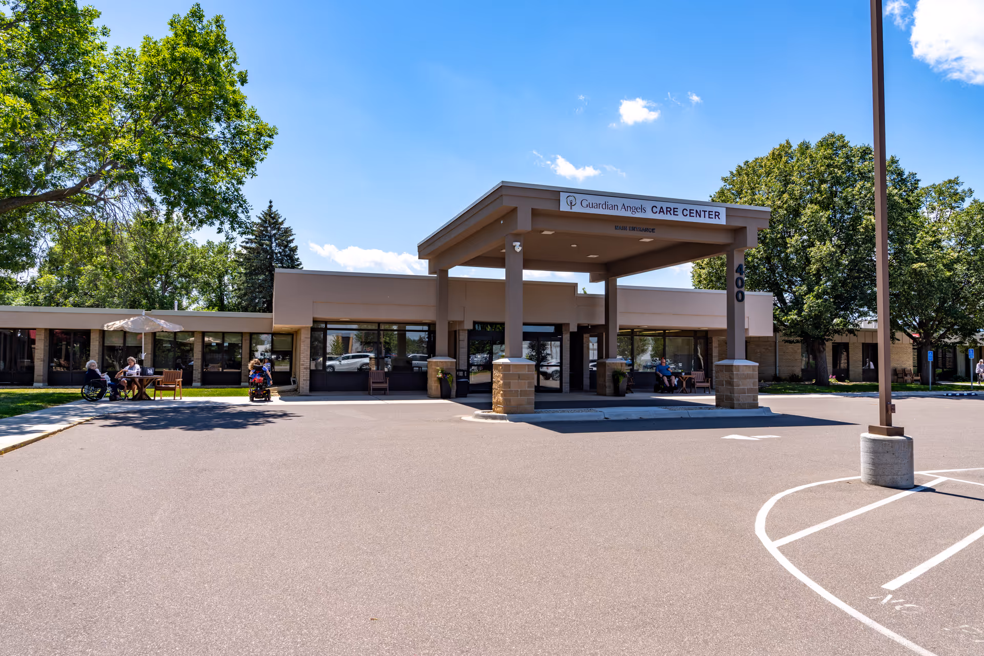 Guardian Angels Care Center front entrance with a covered drop-off and people seated outside.