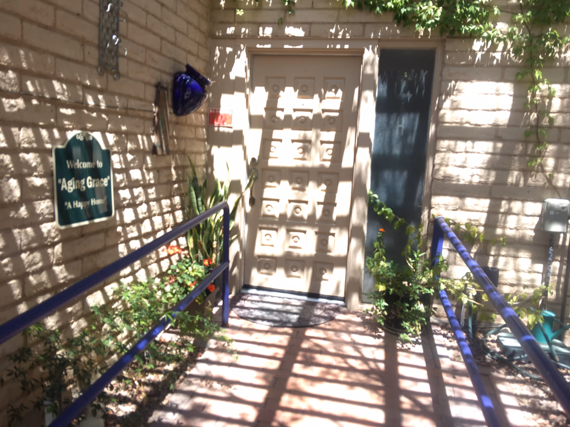 Entrance to Aging Grace facility with brick walls, a door, and potted plants along a ramp.