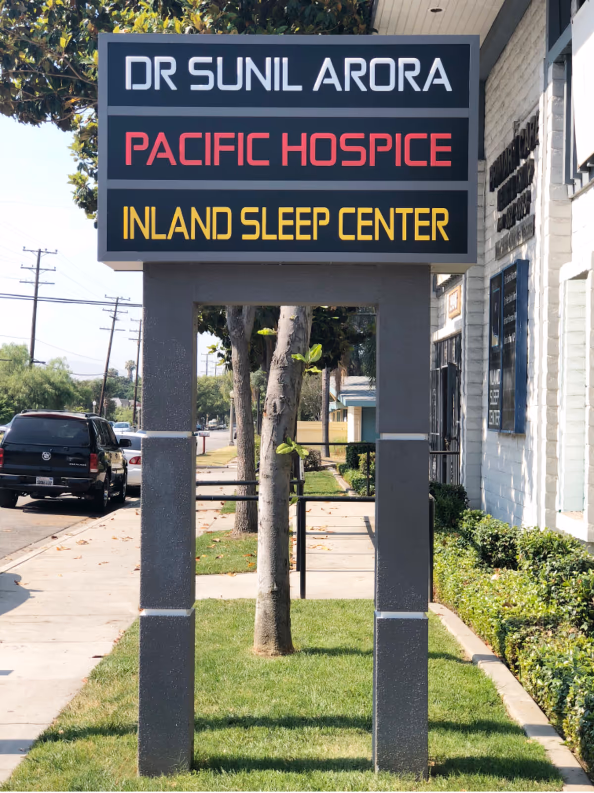 Exterior signboard for Inland Sleep Center and Pacific Hospice beside a sidewalk.