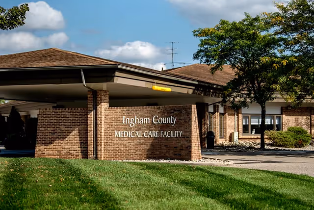 Brick building with a covered entrance and sign reading Ingham County Medical Care Facility.
