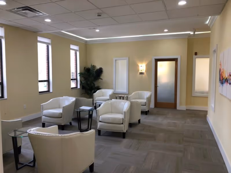 Lounge area in a senior facility with white chairs, glass tables, and warm lighting.