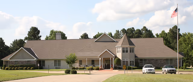 Front view of a single-story senior care home with parking lot and American flag.
