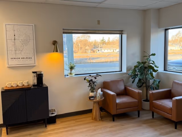 Waiting area with two brown leather chairs, plants, and a coffee station by windows.