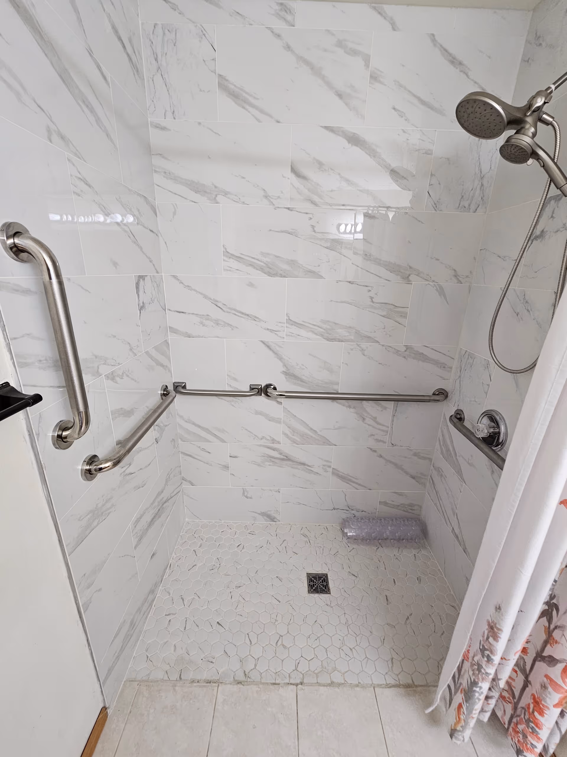 Accessible shower with grab bars, tiled walls, and a drain in a senior living bathroom.