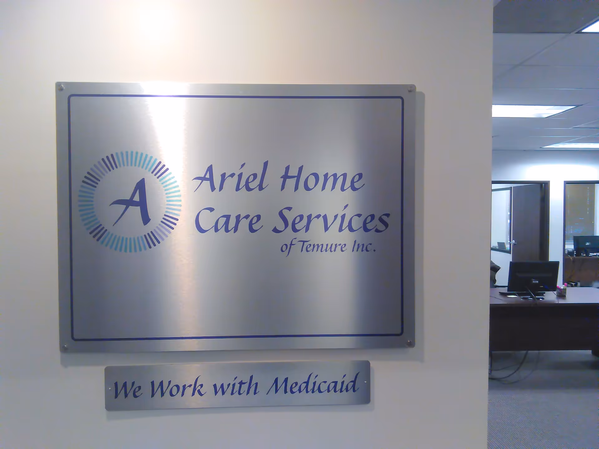 Metal wall plaque reads Ariel Home Care Services with office desks in the background.