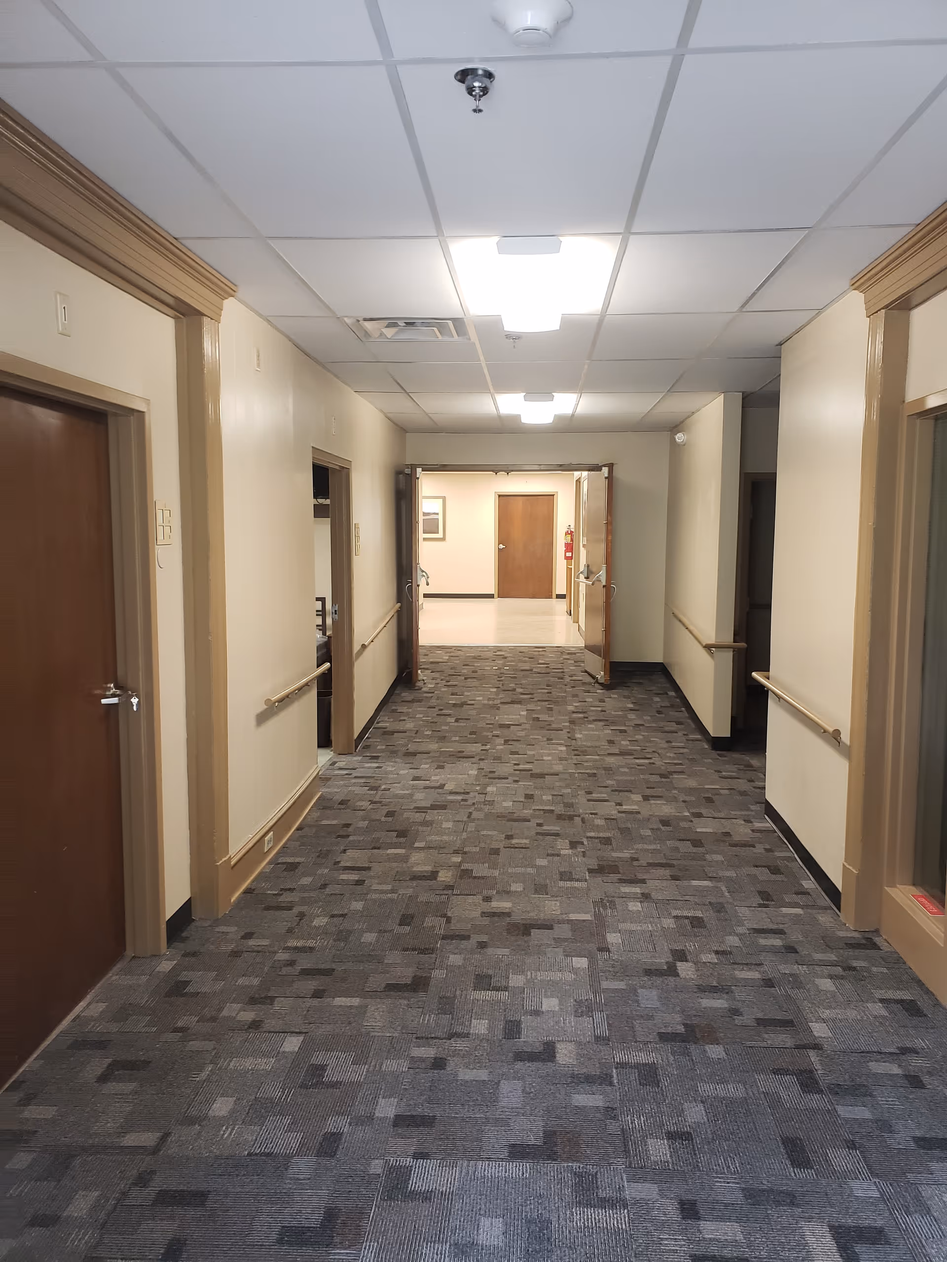 Wide hallway in a senior living facility with doors along both walls and ceiling lights.