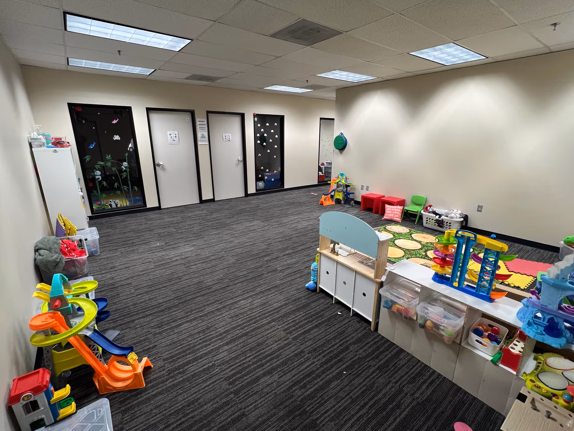Indoor playroom in a facility with colorful toys, storage bins, and classroom doors.