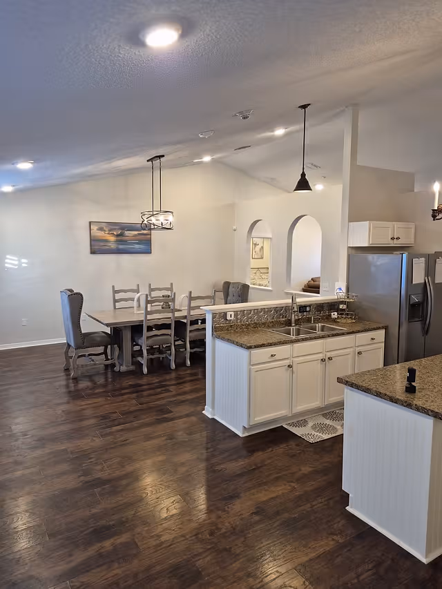 Open kitchen and dining area with island, sink, white cabinets, and dark wood flooring.