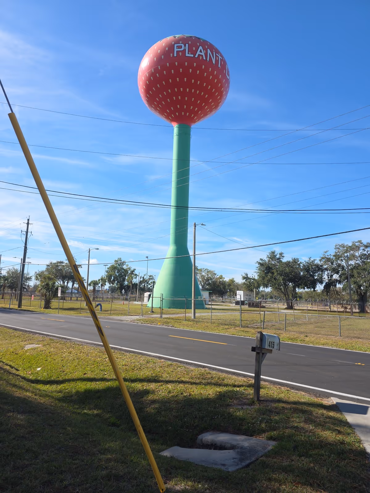 A large green water tower with a red spherical top stands beside a road.