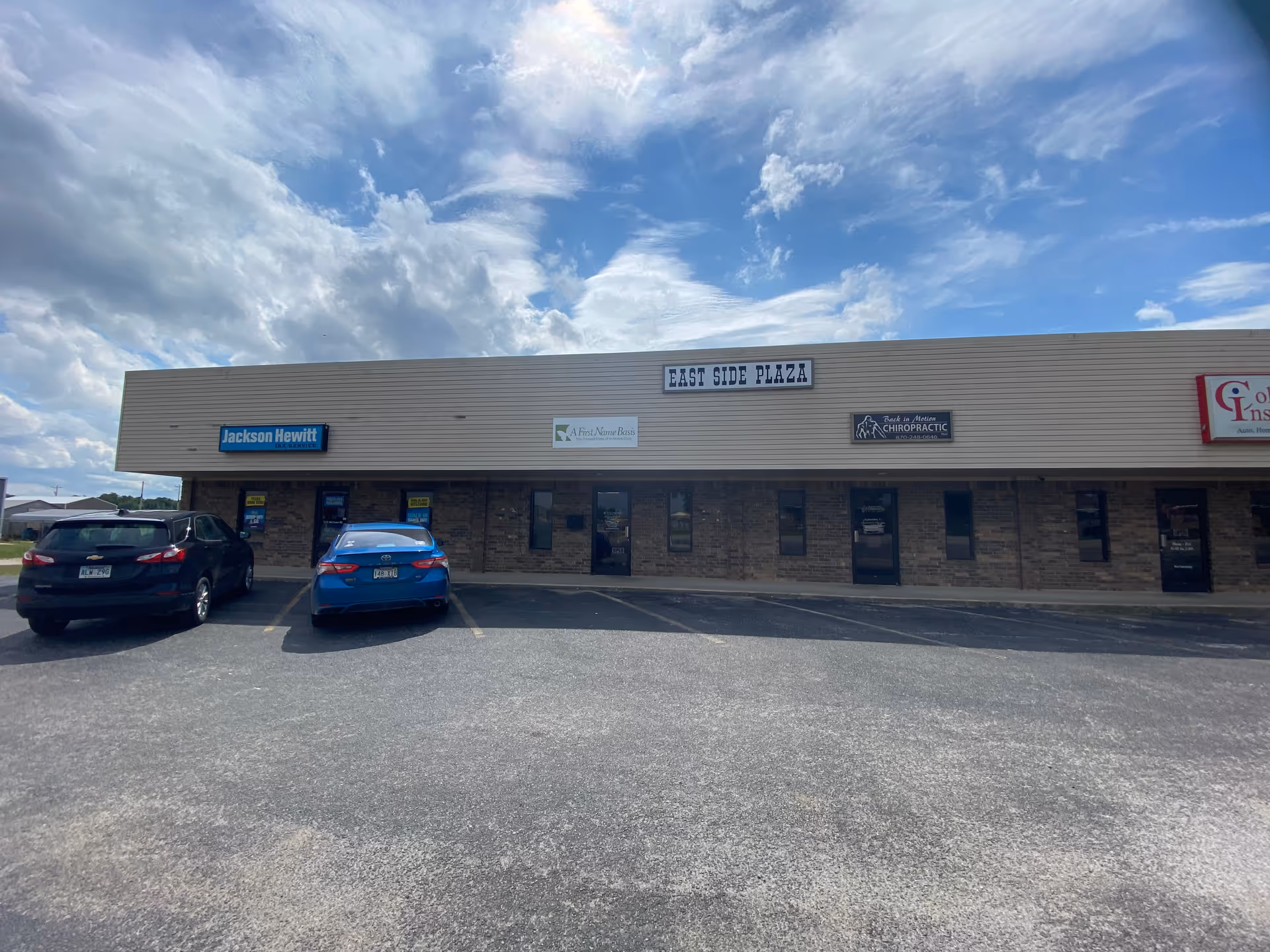 Exterior view of a strip plaza with storefronts and a blue sky.