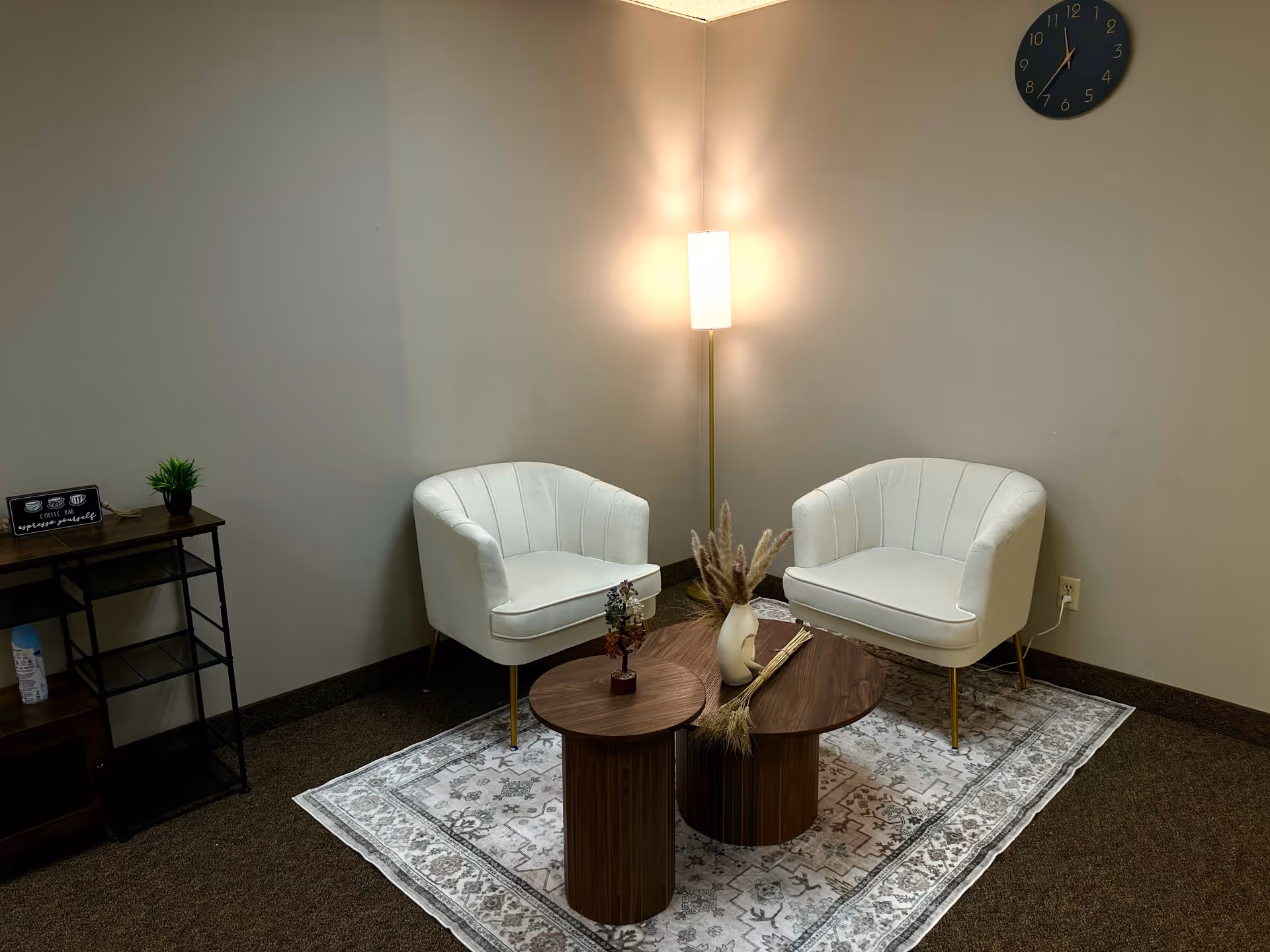 Two white curved chairs flank a round table beneath a floor lamp in a cozy lounge.