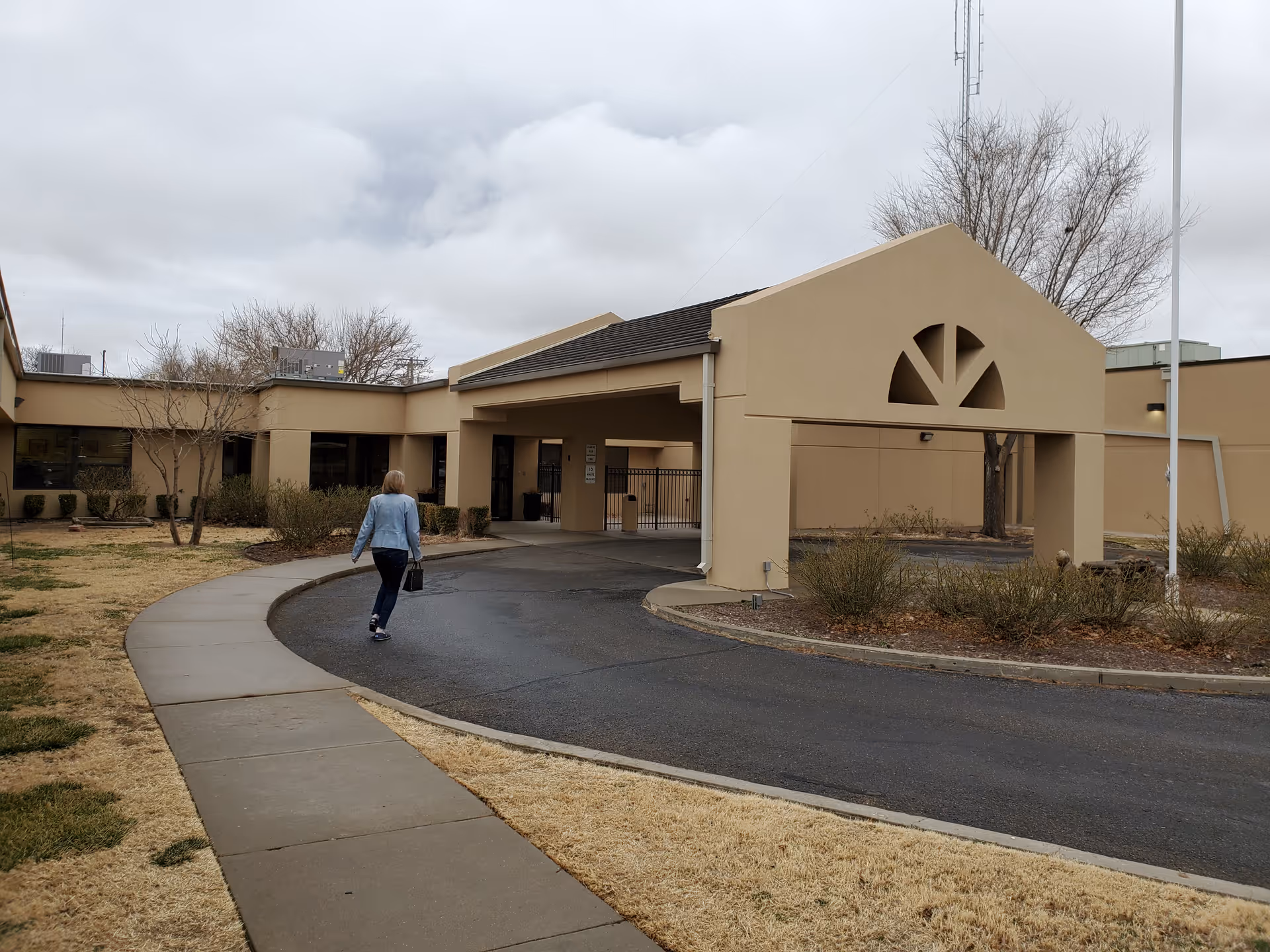Beige senior living facility exterior with curved driveway and a person walking toward the entrance.