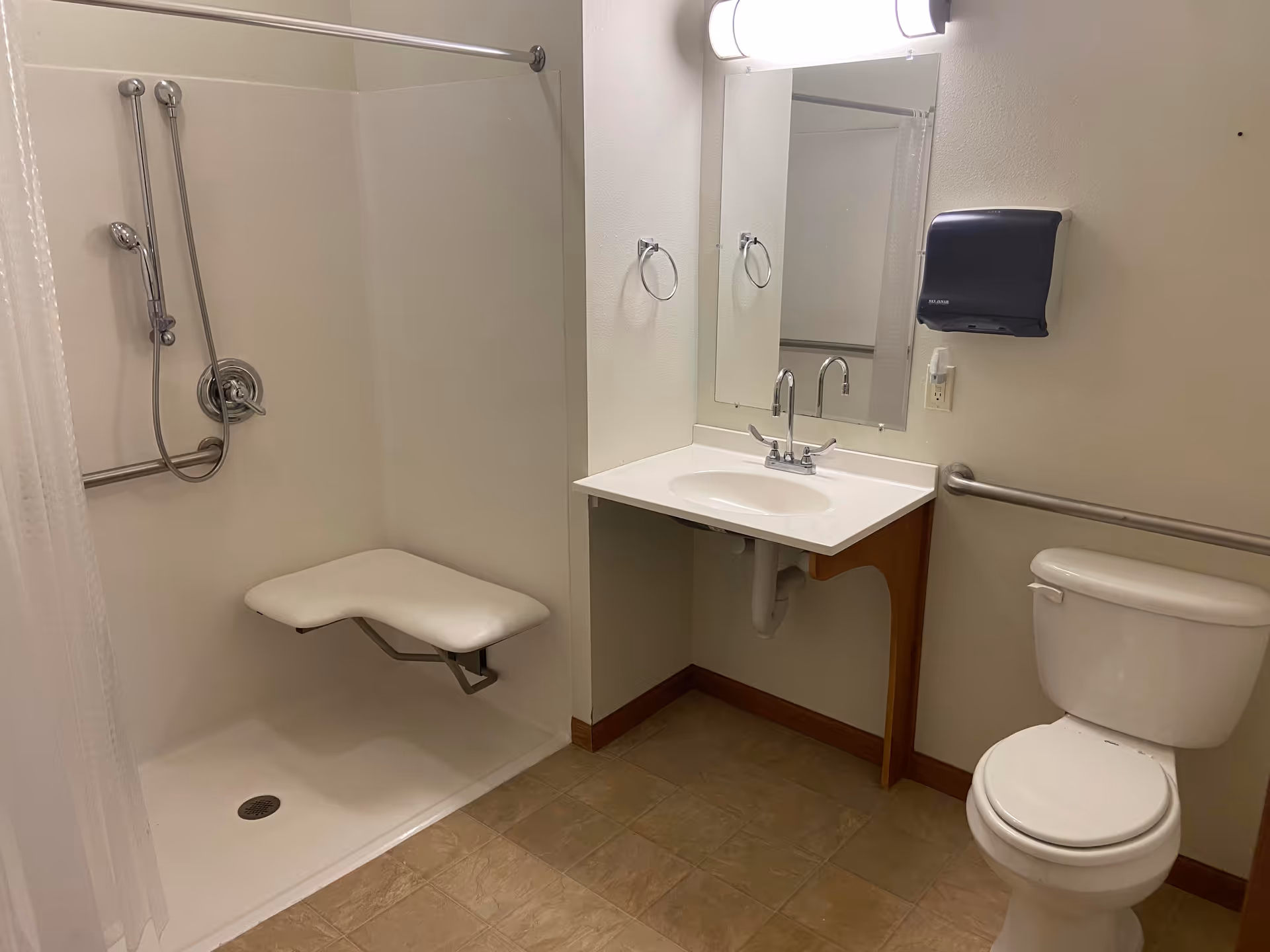 Accessible bathroom with a shower, bench, grab bars, sink, and toilet.