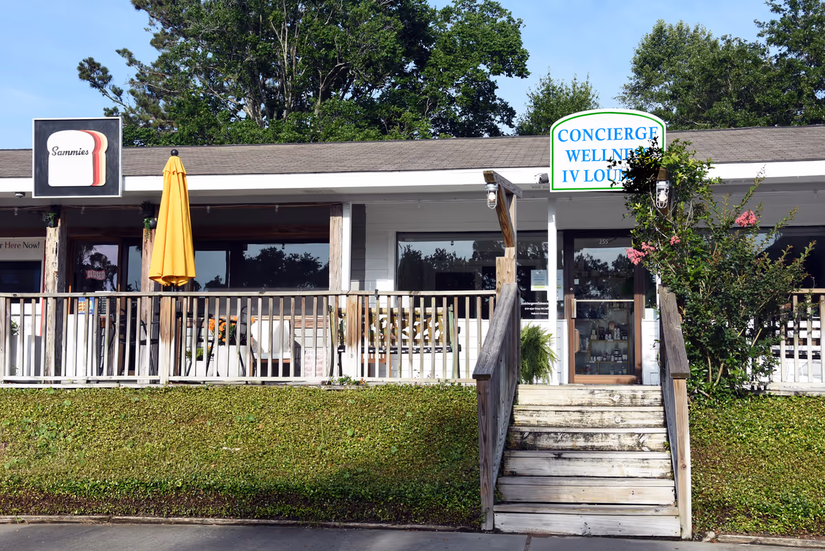 Exterior view of a single-story storefront with a wooden porch and outdoor seating.