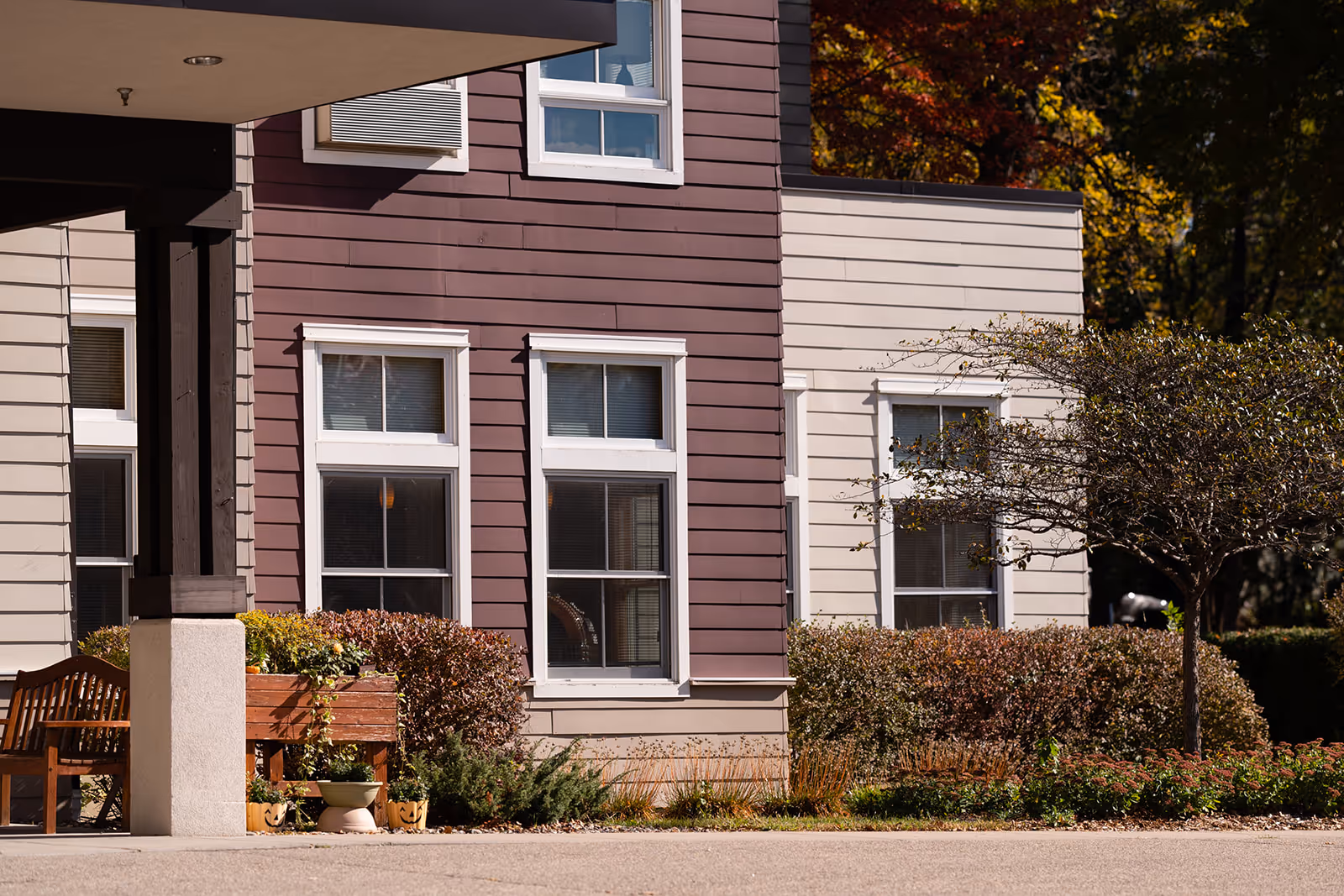 Exterior view of a building facade with multiple windows, siding, a covered entry, bench and landscaping.