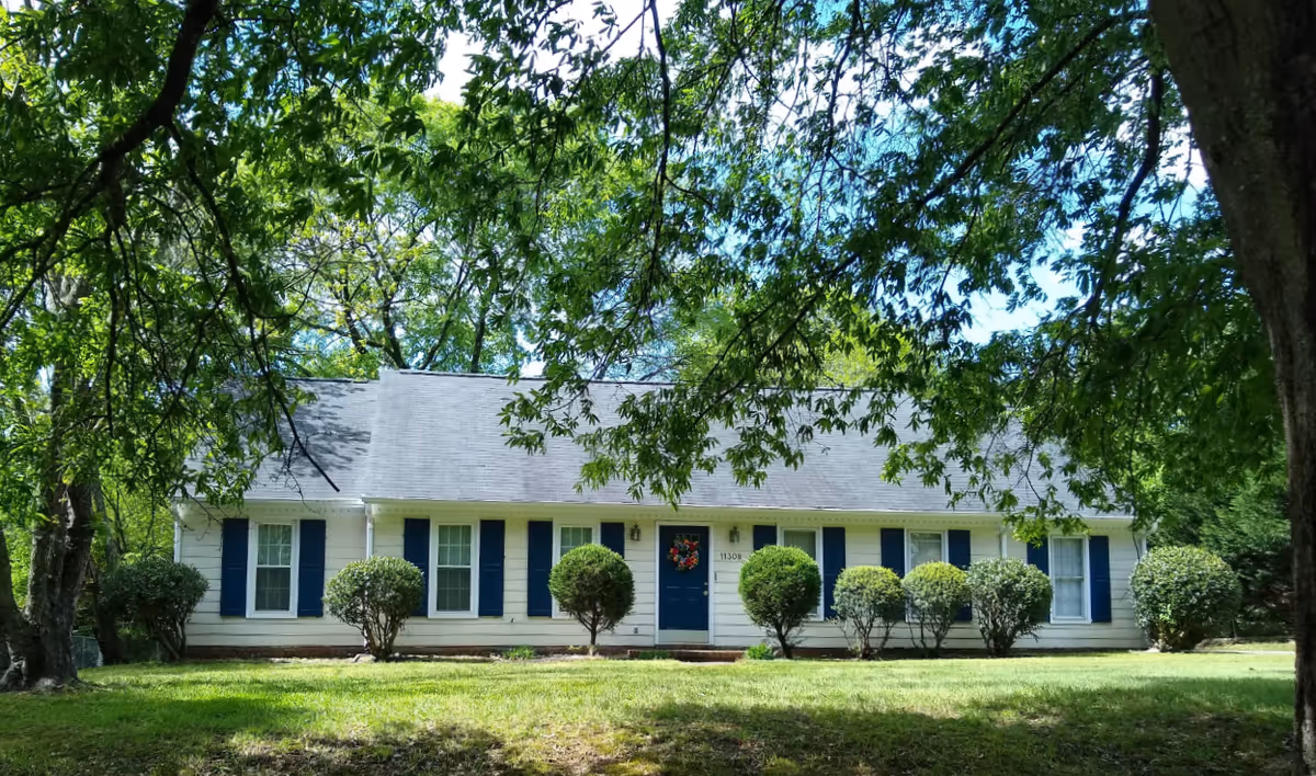 Front view of a single-story white building with blue shutters and a wreath on the door.