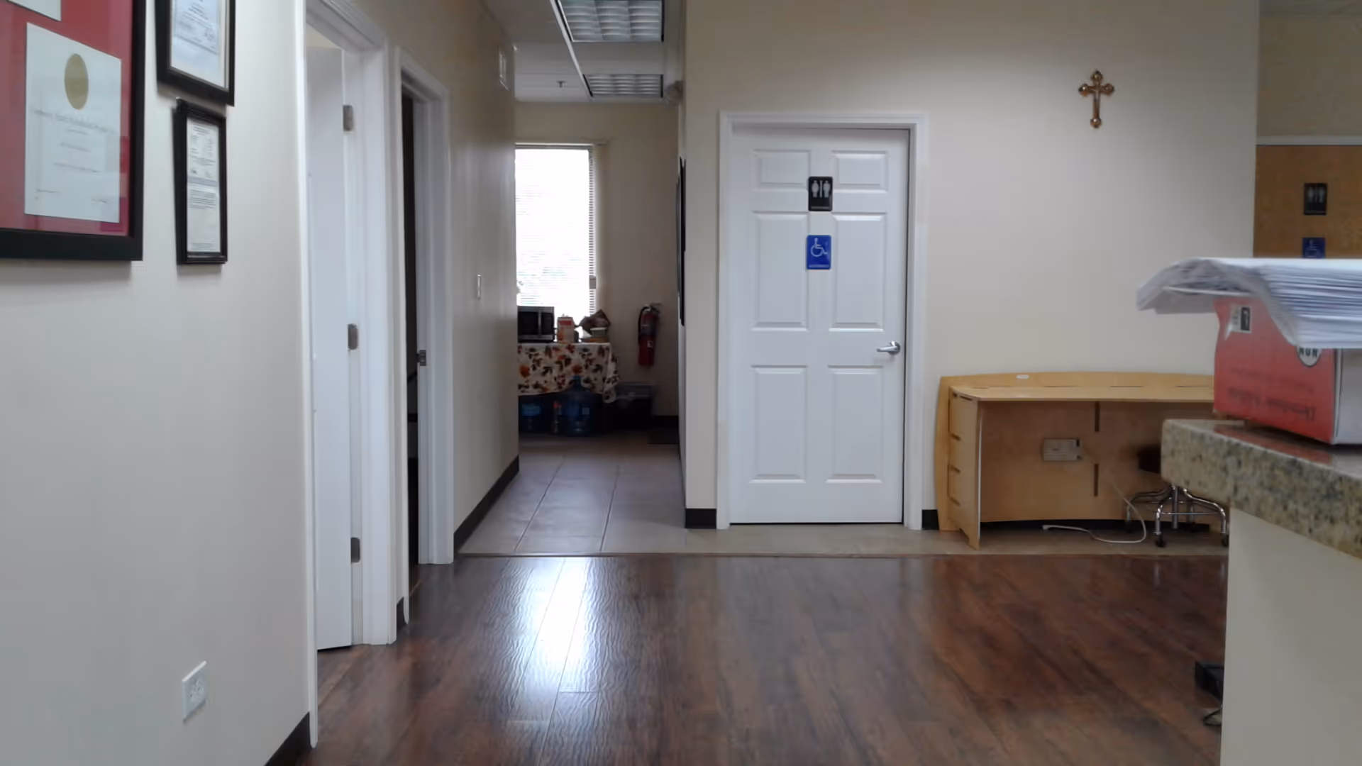 Indoor hallway with a white accessible restroom door, cross on the wall, and a reception counter.