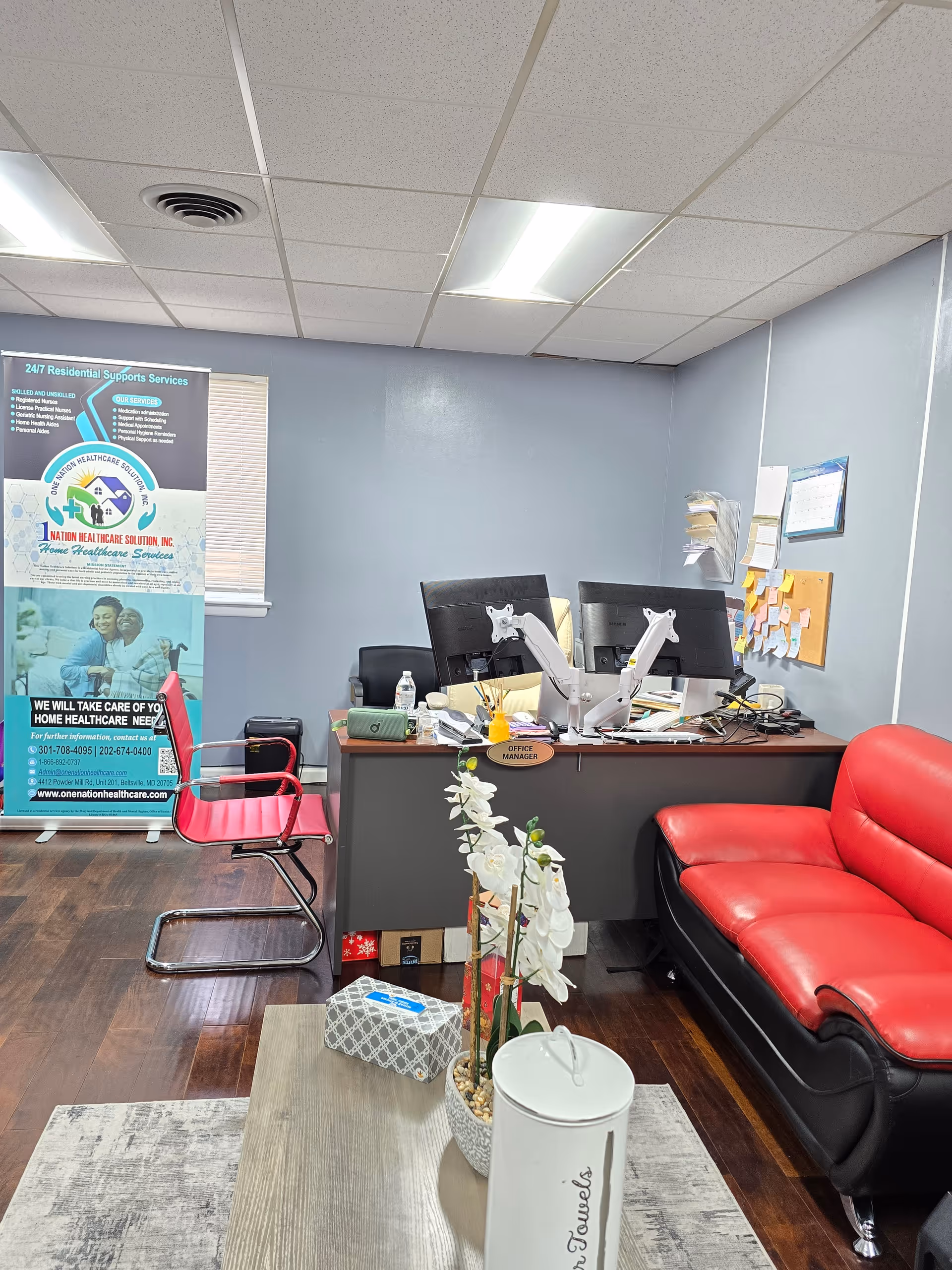 Office reception area with desk, monitors, red sofa, and promotional banner.