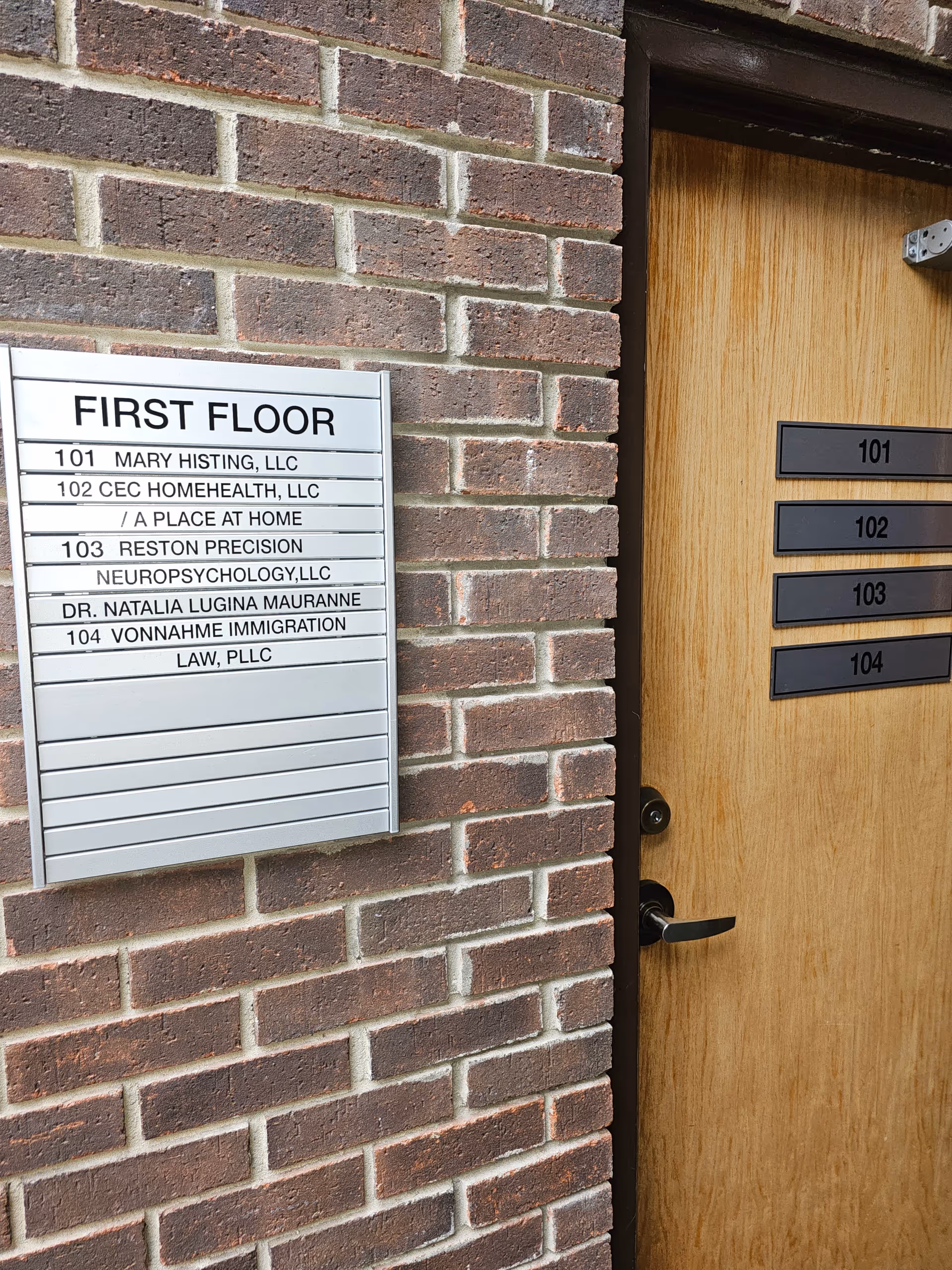 Brick exterior with a first-floor directory sign beside a wooden entry door.