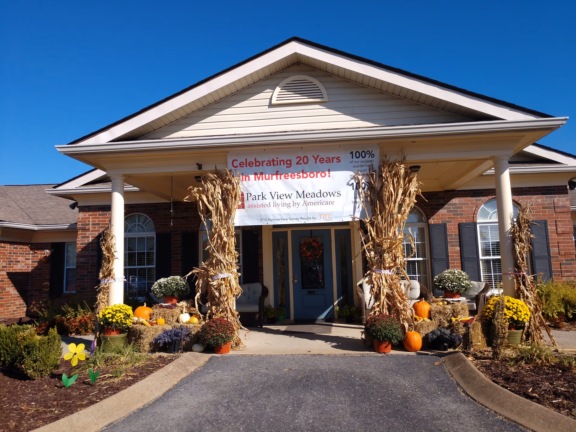 Exterior view of a senior living facility entrance decorated with pumpkins and cornstalks.