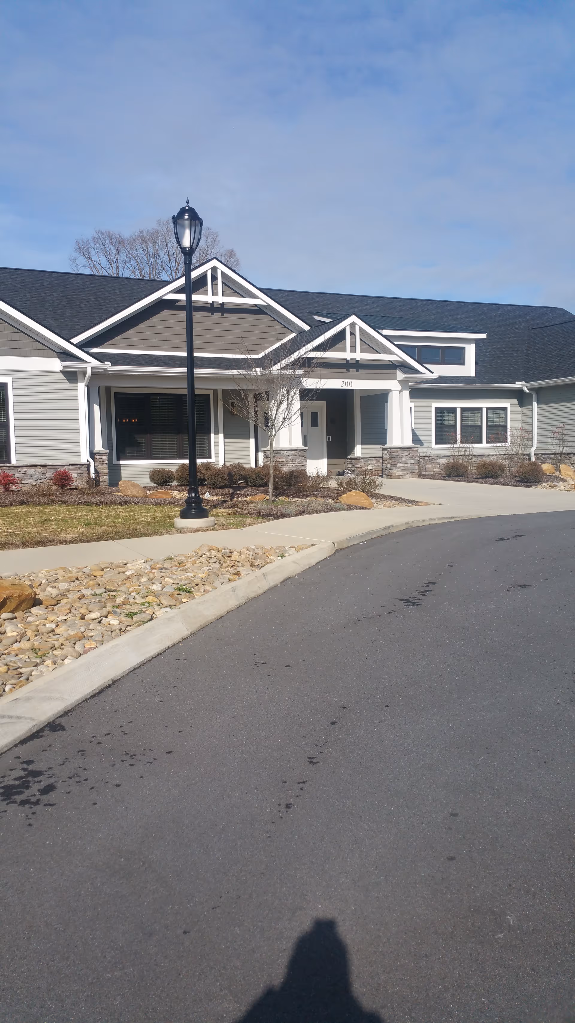 Front exterior of a single-story senior living facility with a lamp post and curved driveway.
