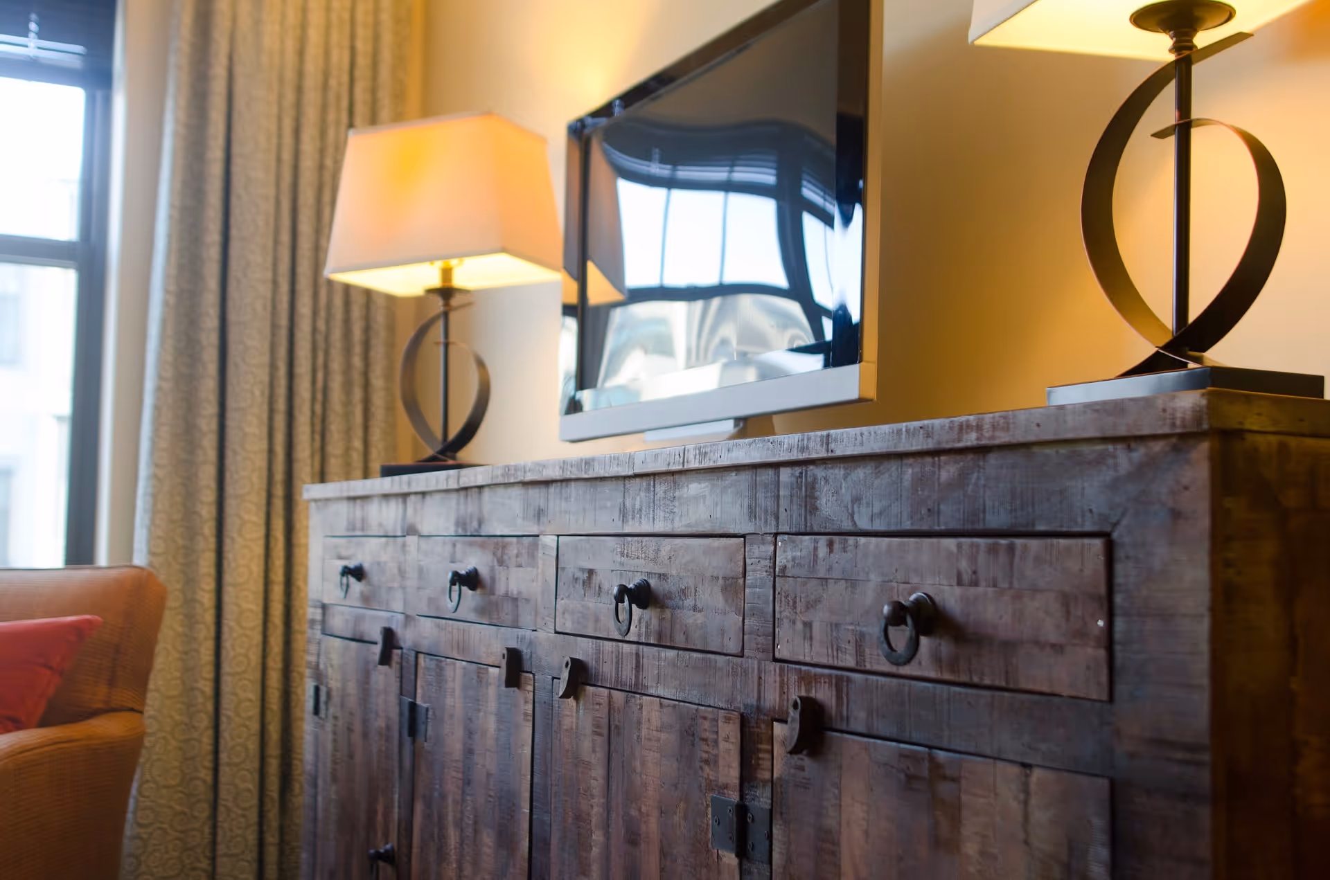 Rustic wooden cabinet with a TV, two lamps, and a sofa in a living room.