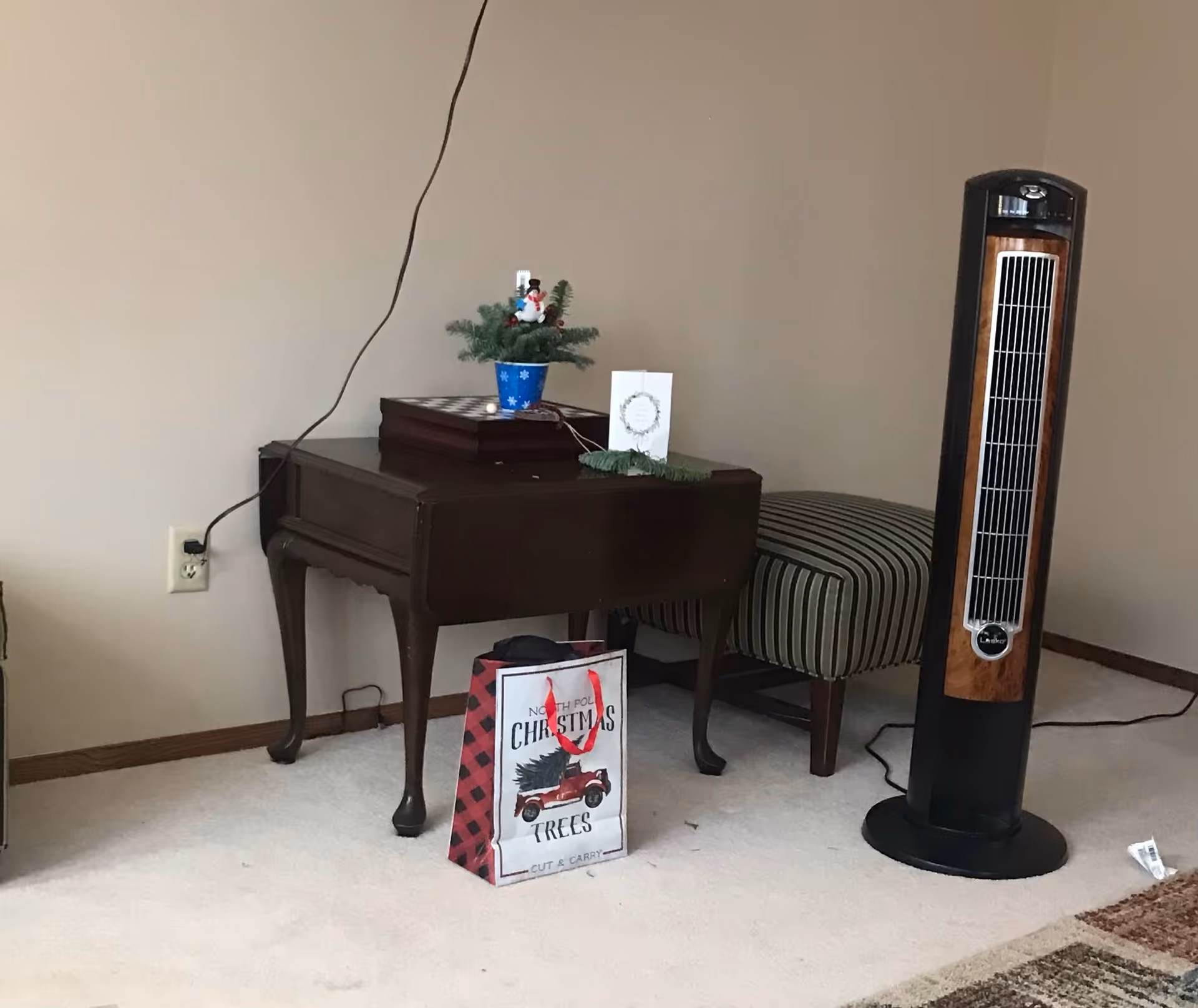 A small living area with a console piano, striped bench, Christmas decorations, and a tall fan.