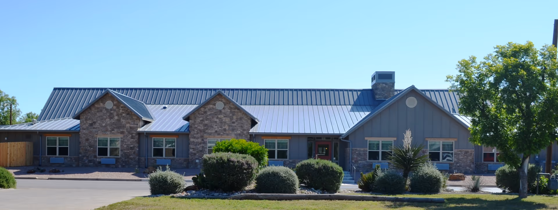 Single-story Crest senior living facility exterior with brick, blue-gray siding, and landscaped shrubs.