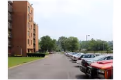 Exterior view of a brick senior living building with a parking lot and trees.