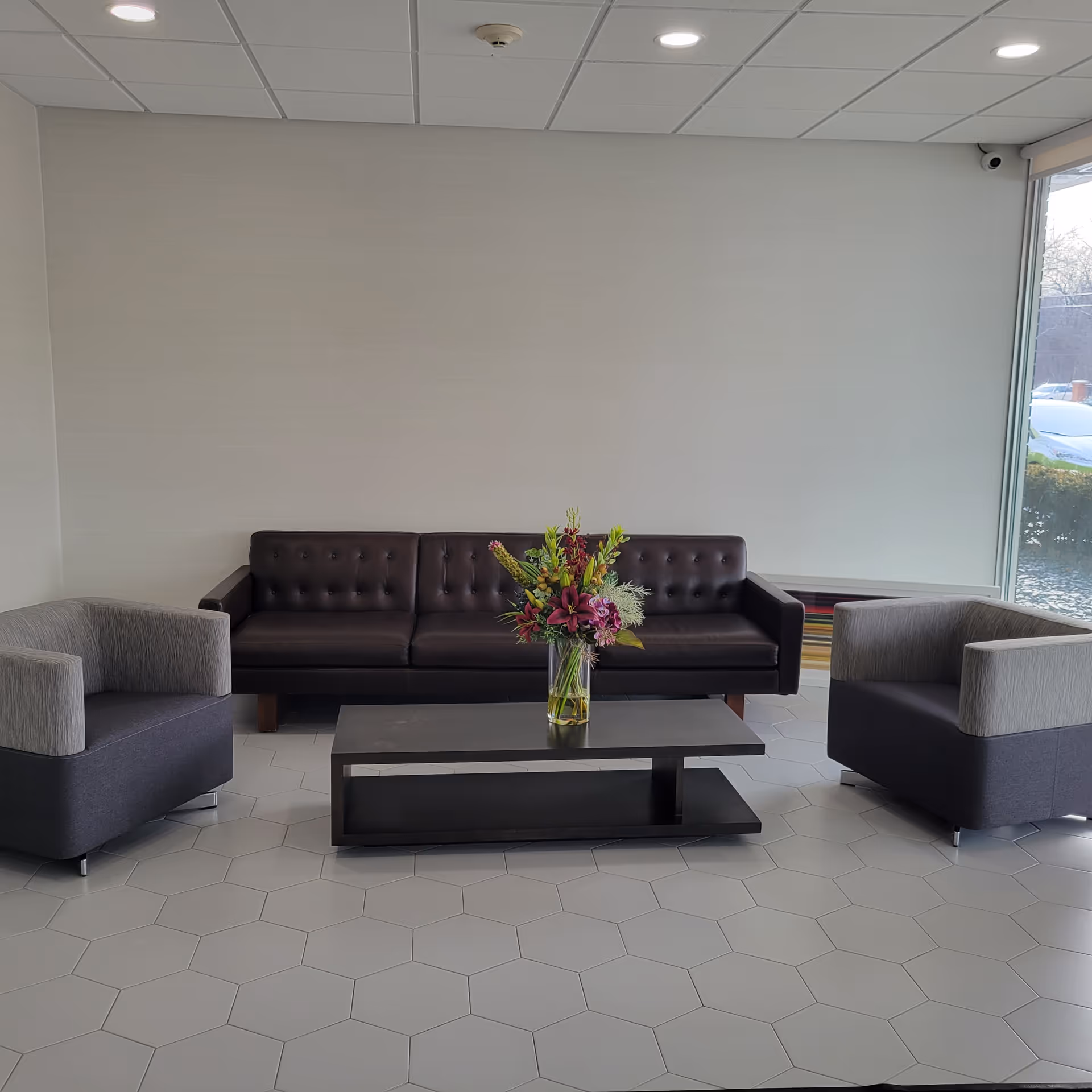 Modern waiting lounge with brown sofa, two armchairs, a coffee table, and a floral arrangement.