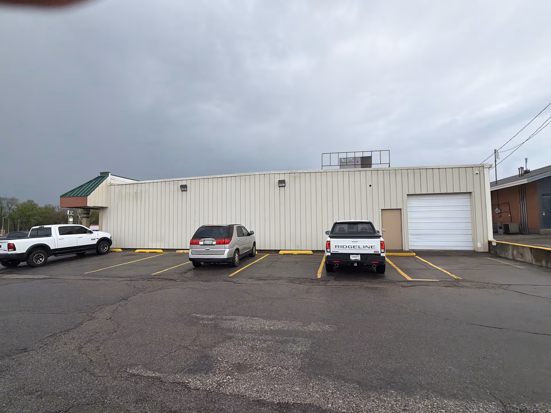 Exterior of a plain beige commercial building with parked vehicles in a parking lot.