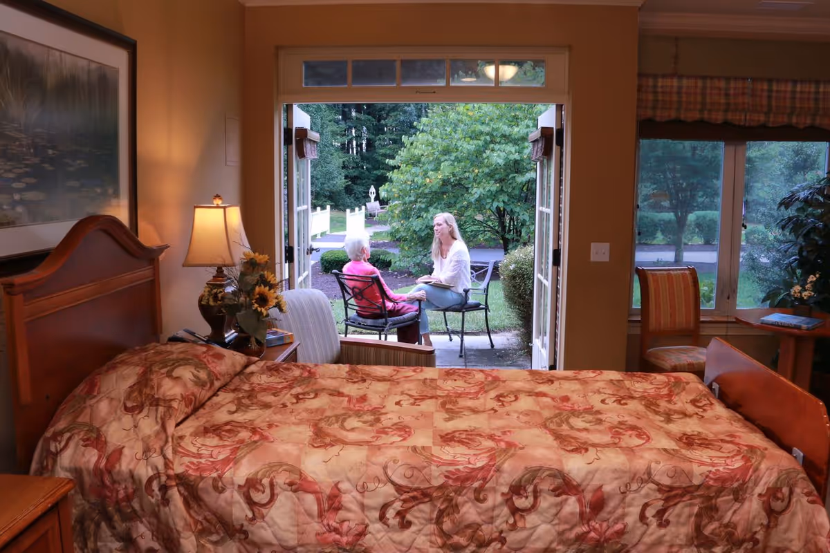 Bedroom with bed facing open doors to patio where two people converse.