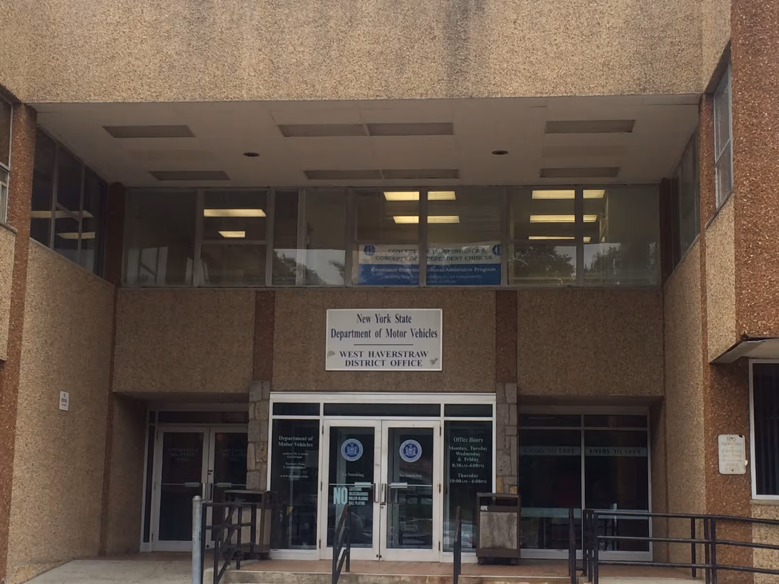 Front entrance of a brick building with glass doors and a New York DMV sign.