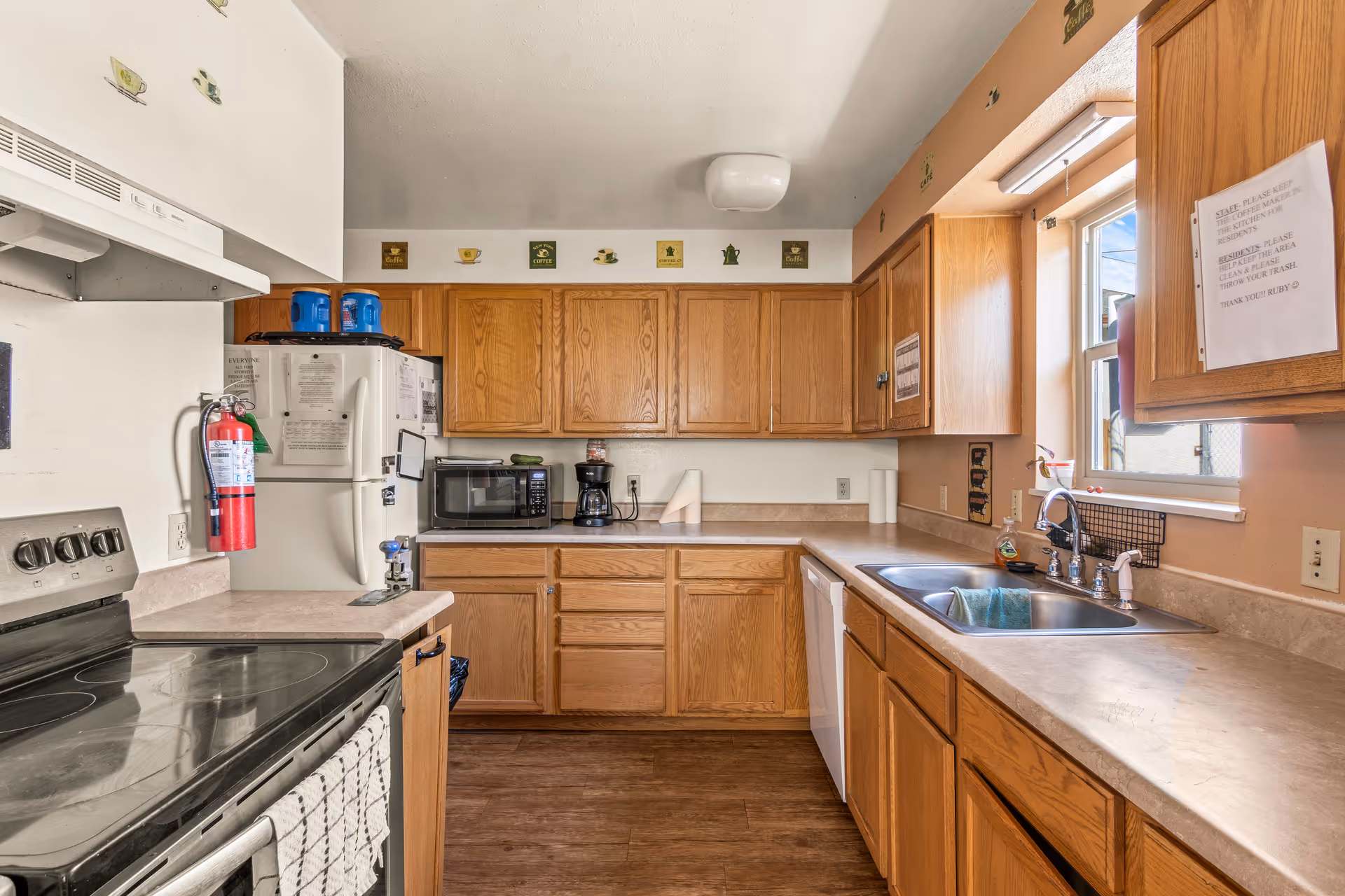 Compact kitchen with wooden cabinets, stove, refrigerator, sink, microwave, and coffee maker.