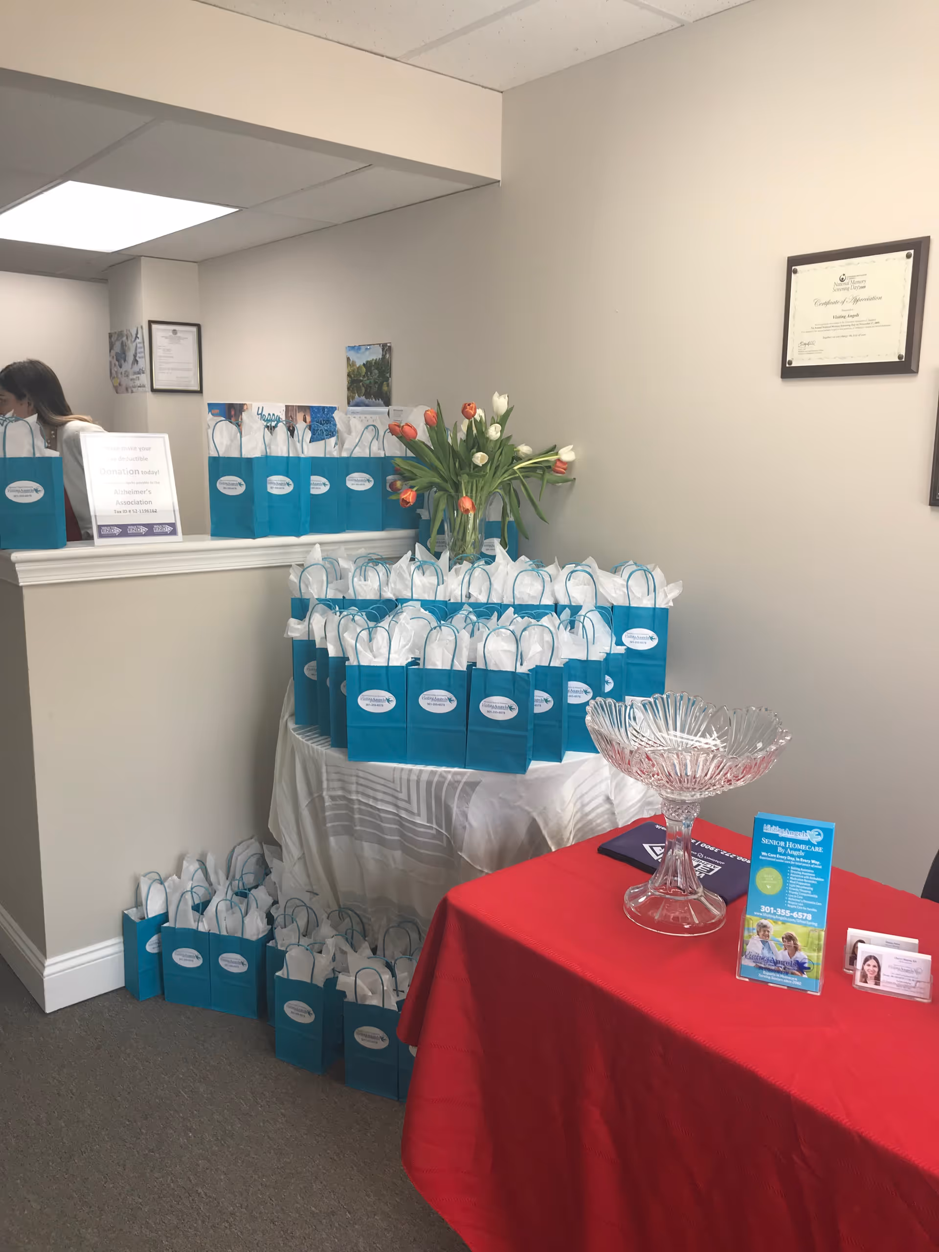 Reception area with teal gift bags arranged on tables and a red-draped display.