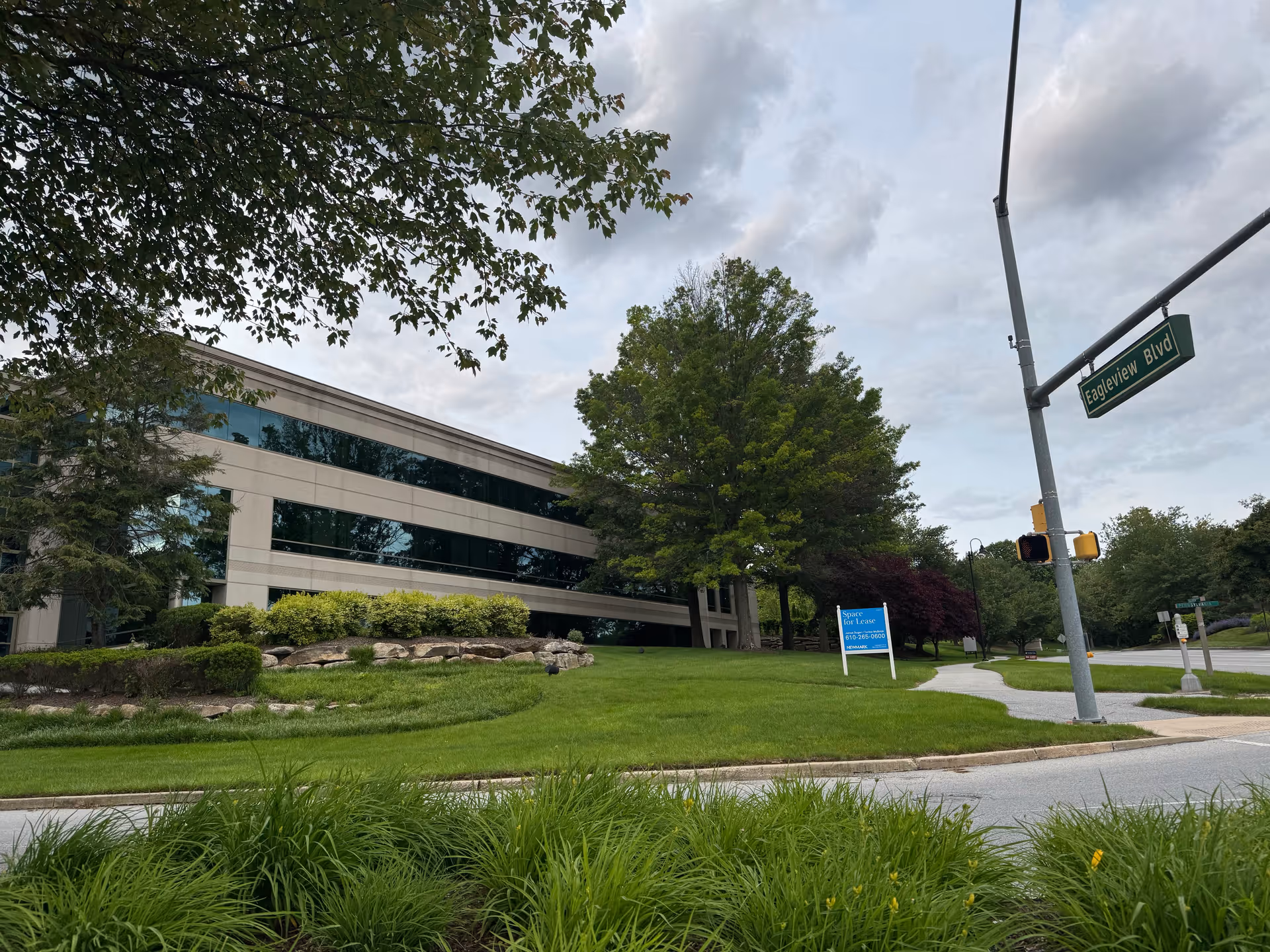 Modern office-style building with glass windows, green lawn, trees, and a street sign.