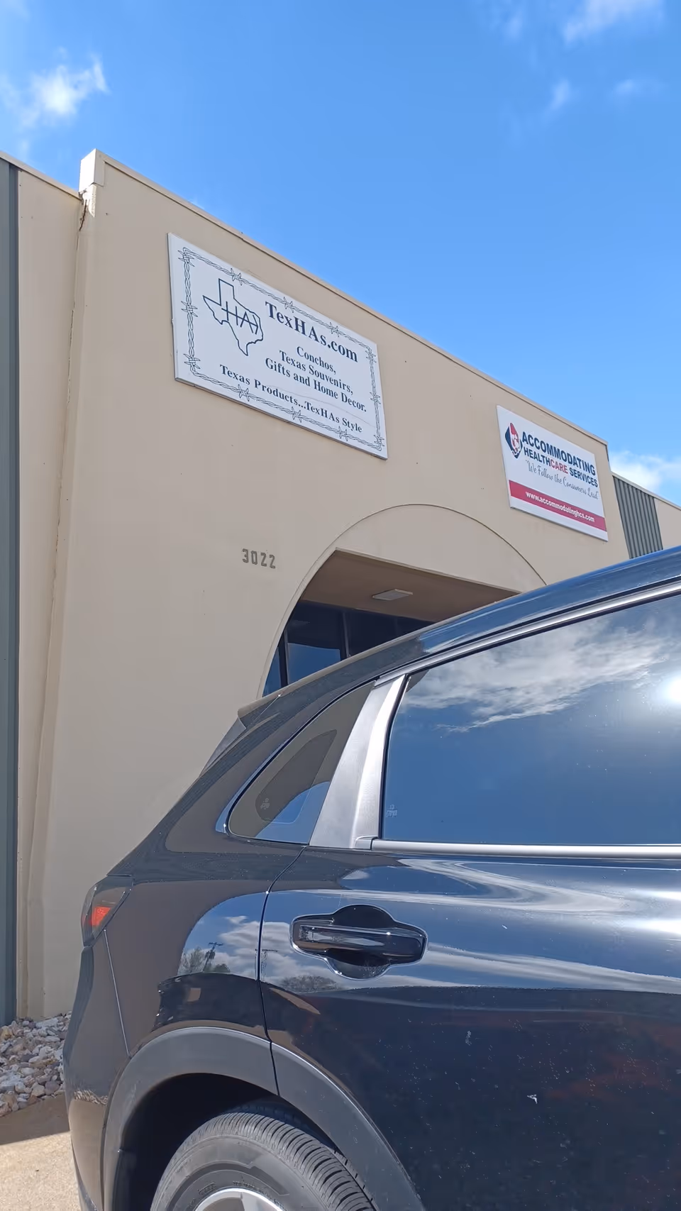 A beige building entrance with signs and a parked dark SUV in front.