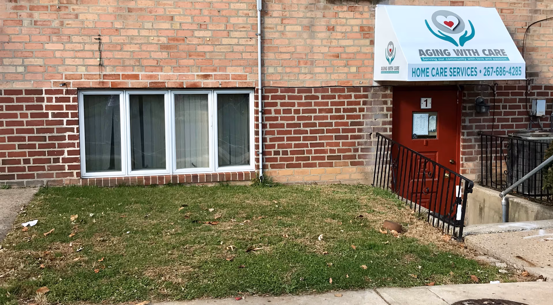 Brick facility exterior with a sign reading Aging With Care and a red entry door.